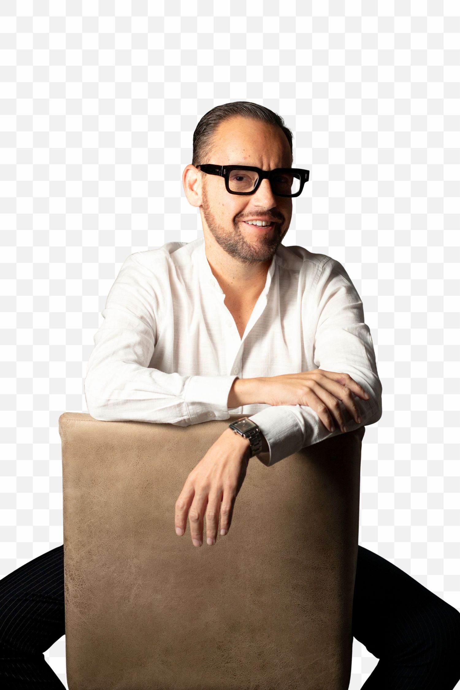 Professional wearing glasses and a white shirt smiles while leaning on a brown chair in a studio setting.