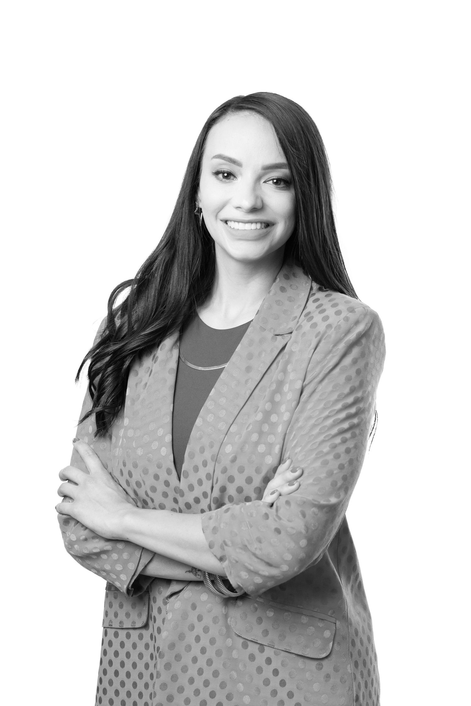 Professional black and white portrait of a woman in polka dot blazer with arms crossed and warm smile.