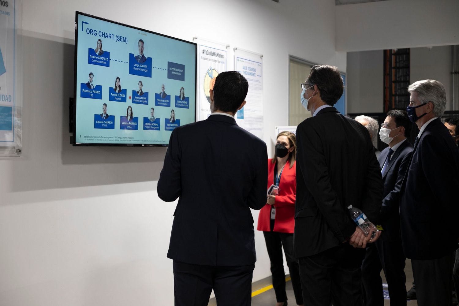 Business professionals in suits viewing an organizational chart displayed on a large screen monitor in an office.