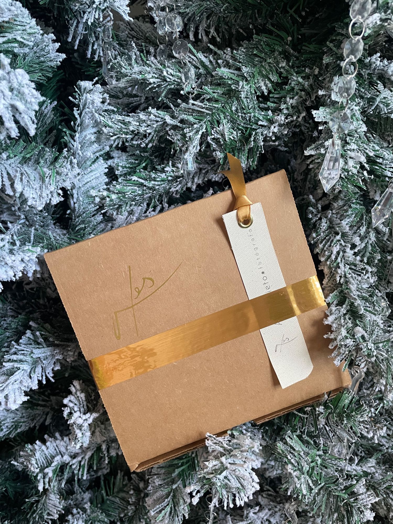 Blank kraft paper gift tags with gold washi tape hang against a snowy white flocked Christmas tree background.