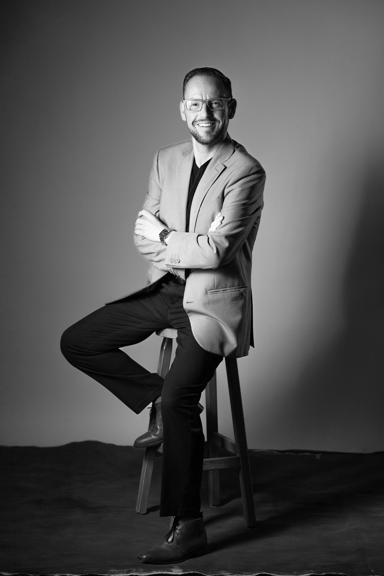 Black and white portrait series showing a person in a light suit jacket posing expressively while seated on a chair.