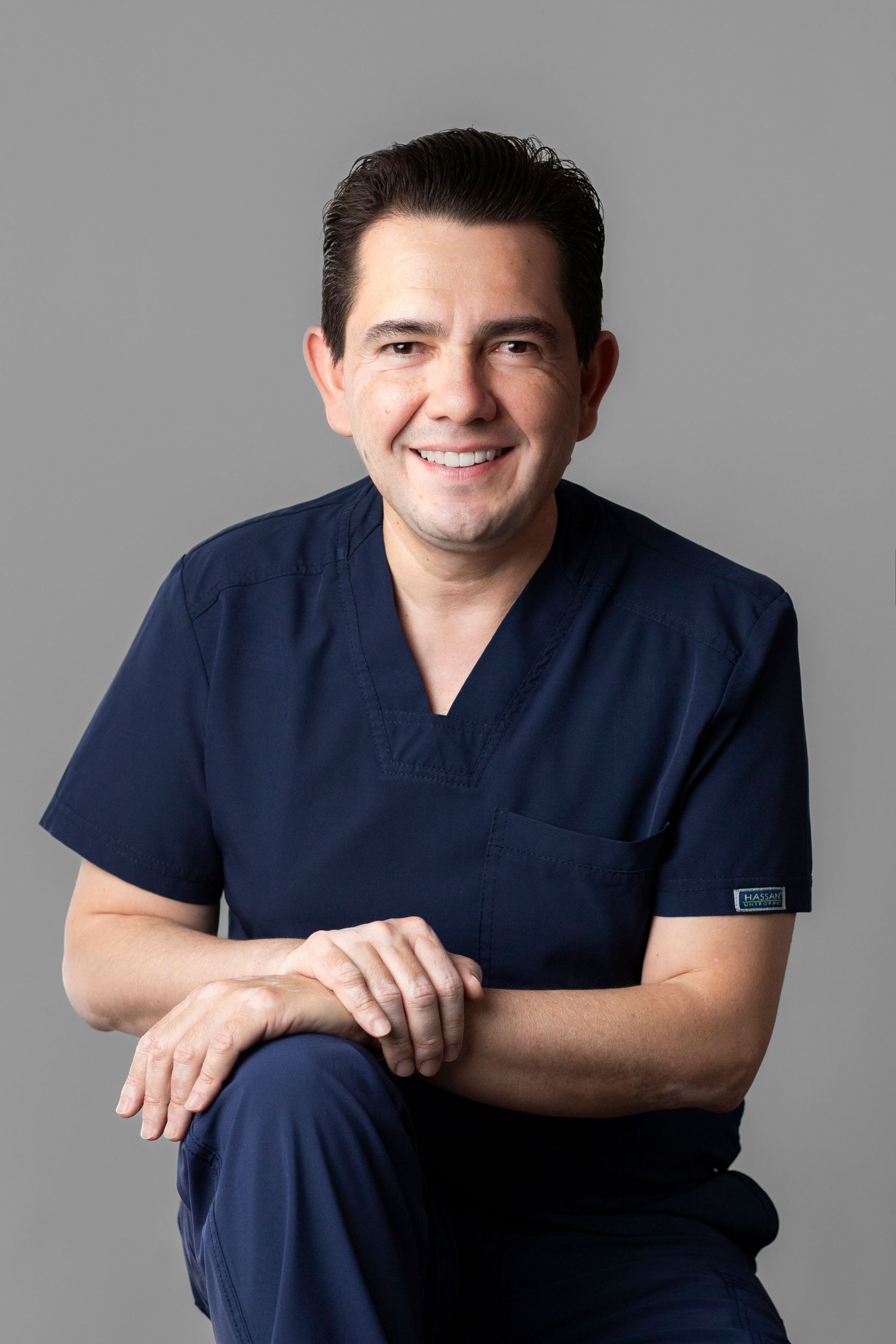 A series of professional headshots showing someone in navy blue medical scrubs against a neutral gray background.