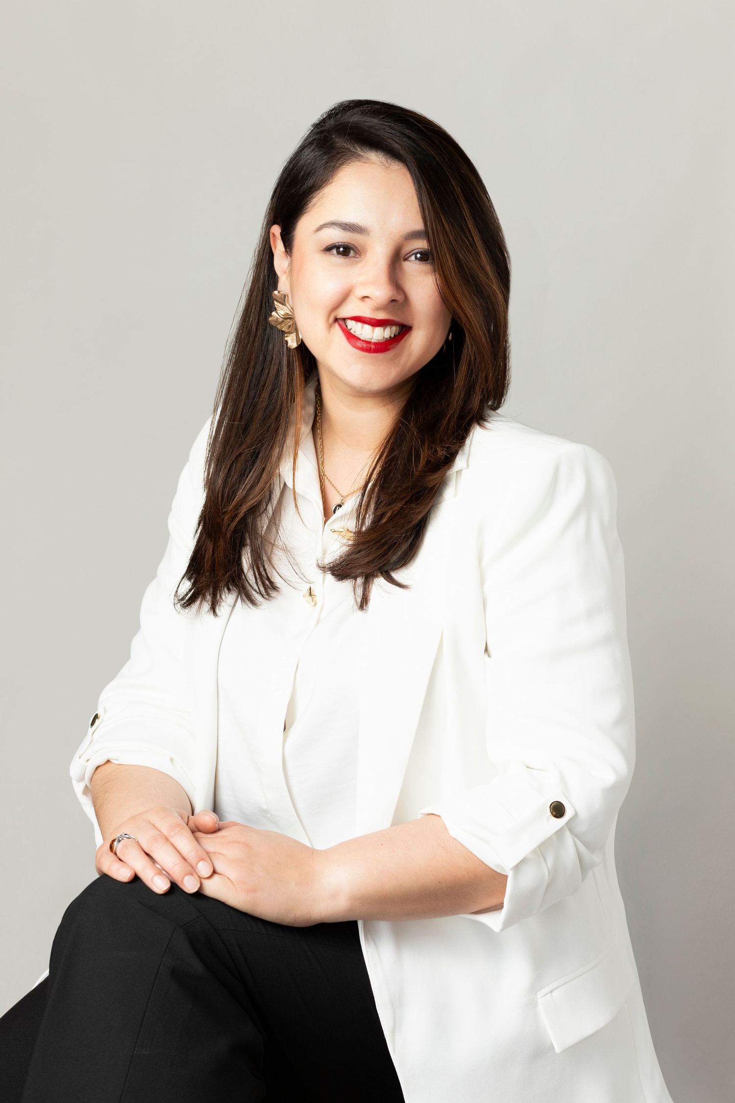Professional studio portraits of someone in a crisp white blazer and dark bottom against a light gray background.