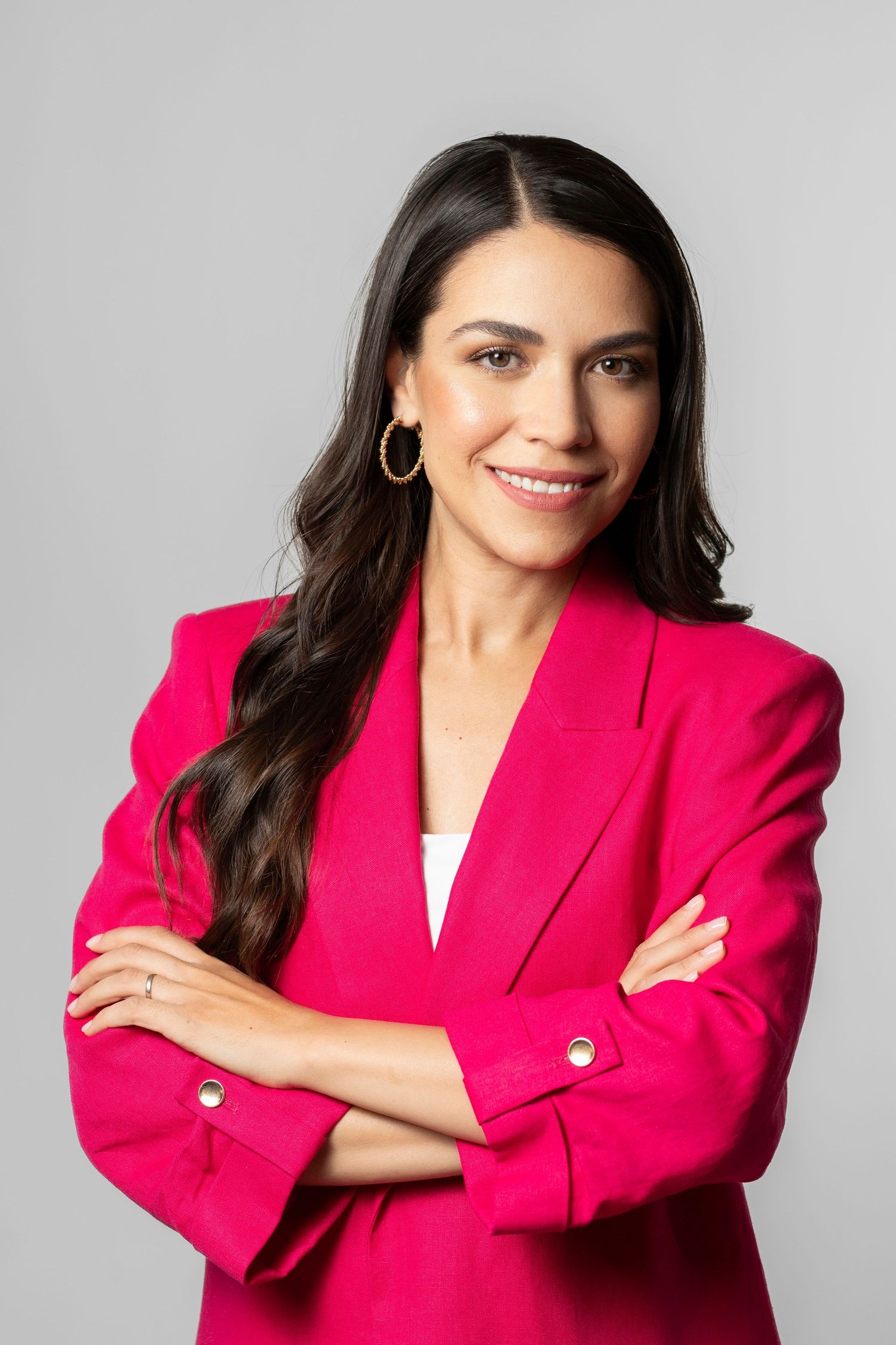 Professional studio portrait of someone wearing a vibrant hot pink blazer with gold buttons against a light gray background.