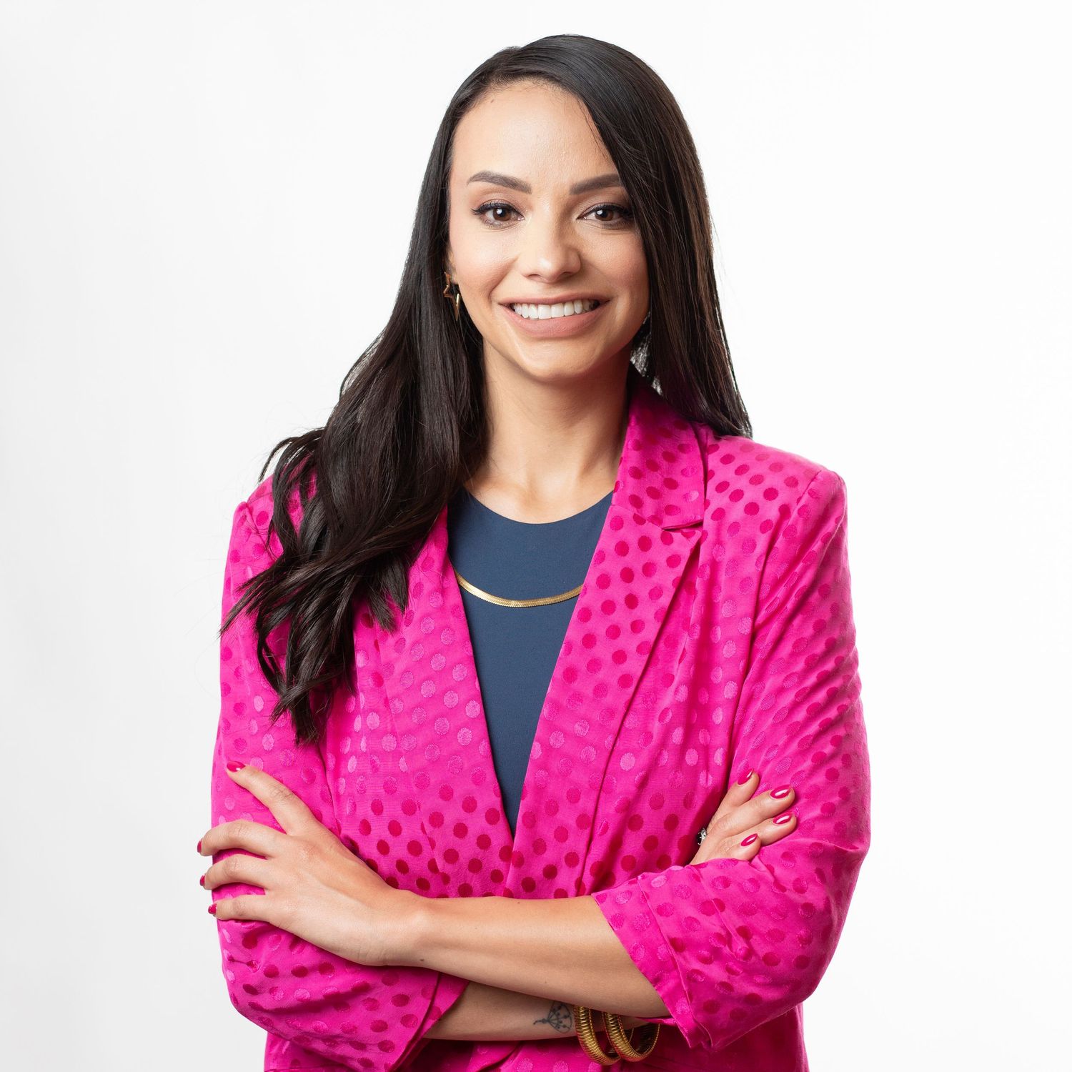 Professional portrait of someone in a bright pink textured blazer and navy top smiling with arms crossed.
