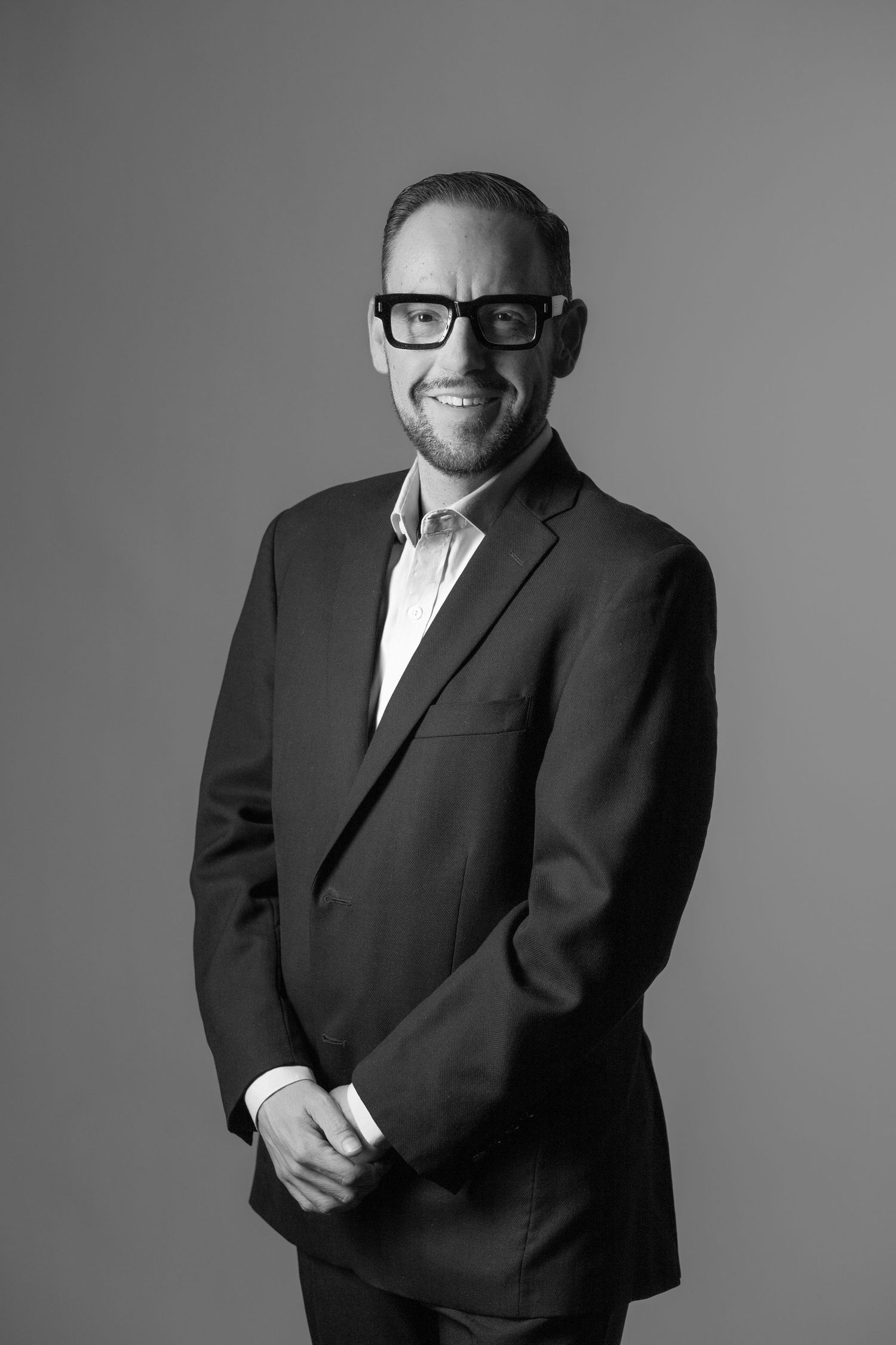 Professional black and white portrait series showing a person in a suit smiling and posing against a gray backdrop.