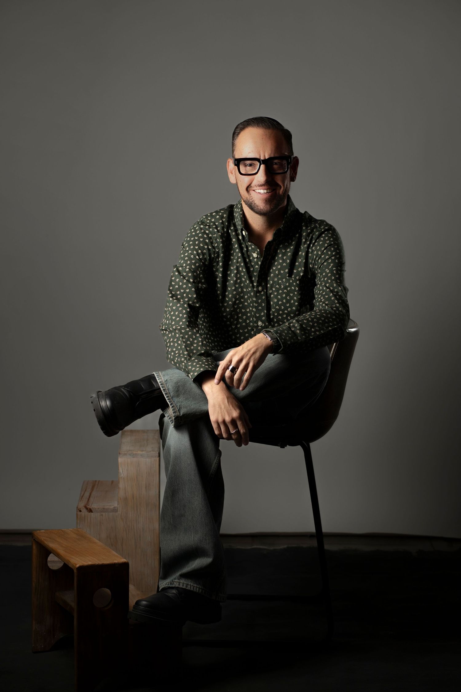A series of moody portrait photographs showing a person in a polka dot shirt sitting casually in a dark chair against a gray backdrop.