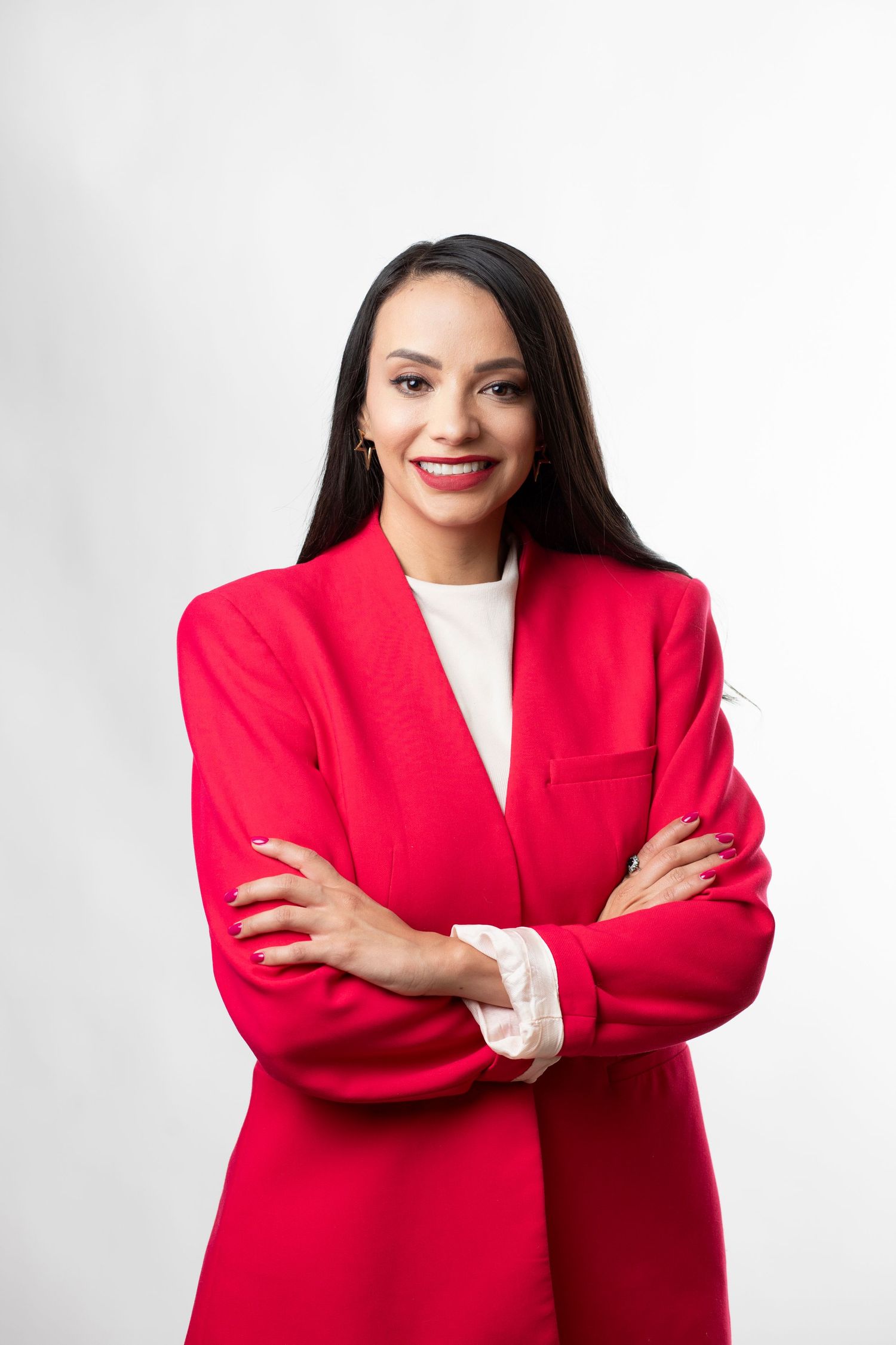 Confident pose in bright red blazer with crossed arms against clean white backdrop.