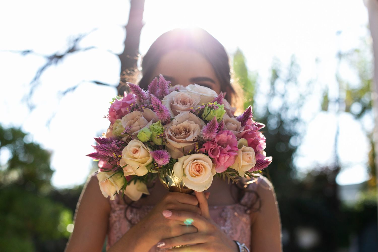A colorful bridal bouquet held up against bright sunlight with pink and peach blooms.