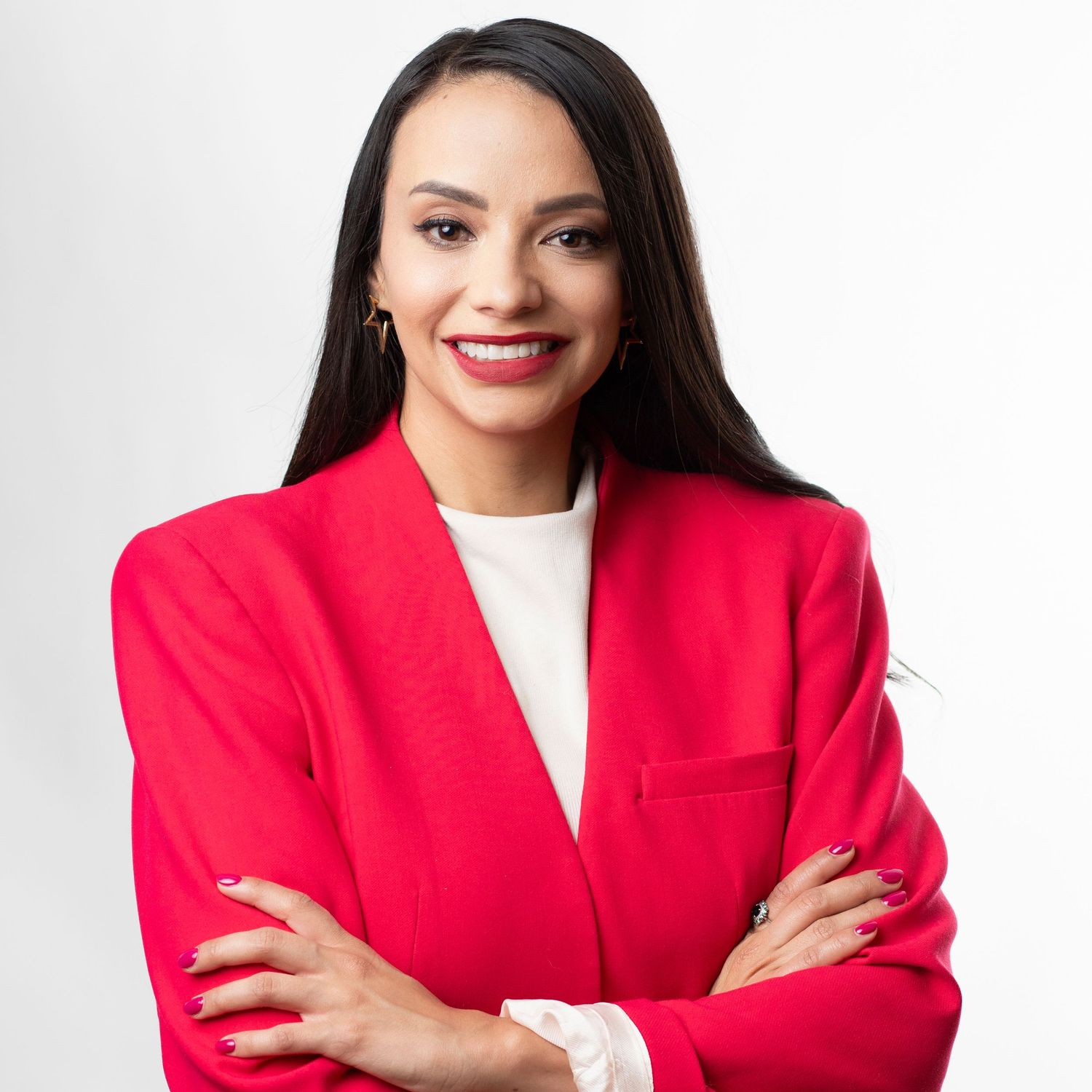 Woman wearing vibrant red blazer and white top poses confidently with crossed arms against white backdrop.