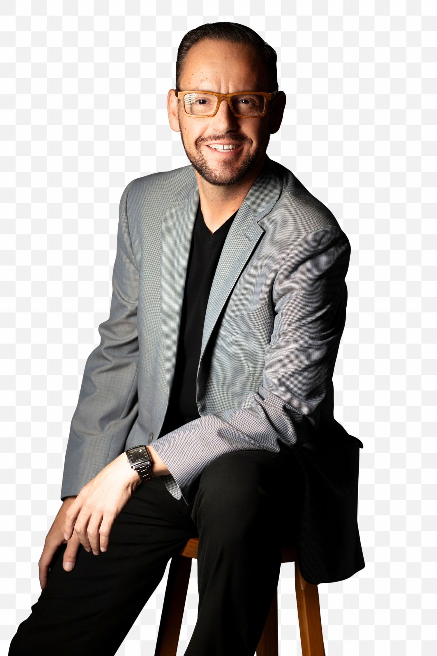 Professional portrait of someone in a gray blazer and black v-neck shirt sitting on a stool against white background.