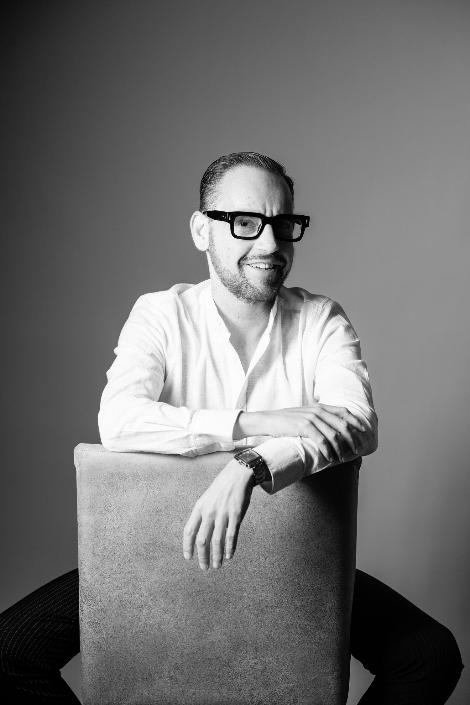 Black and white portrait series showing someone in a white shirt leaning on a chair with varying poses and expressions.