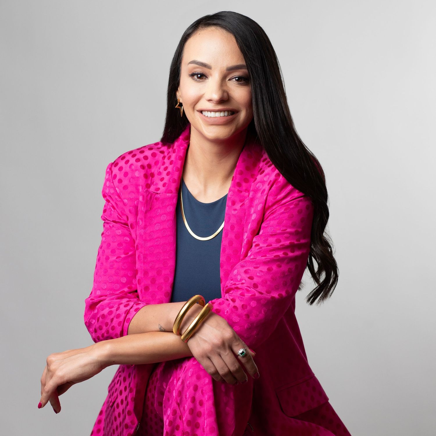 Professional wearing a vibrant hot pink textured blazer poses against a gray studio backdrop.