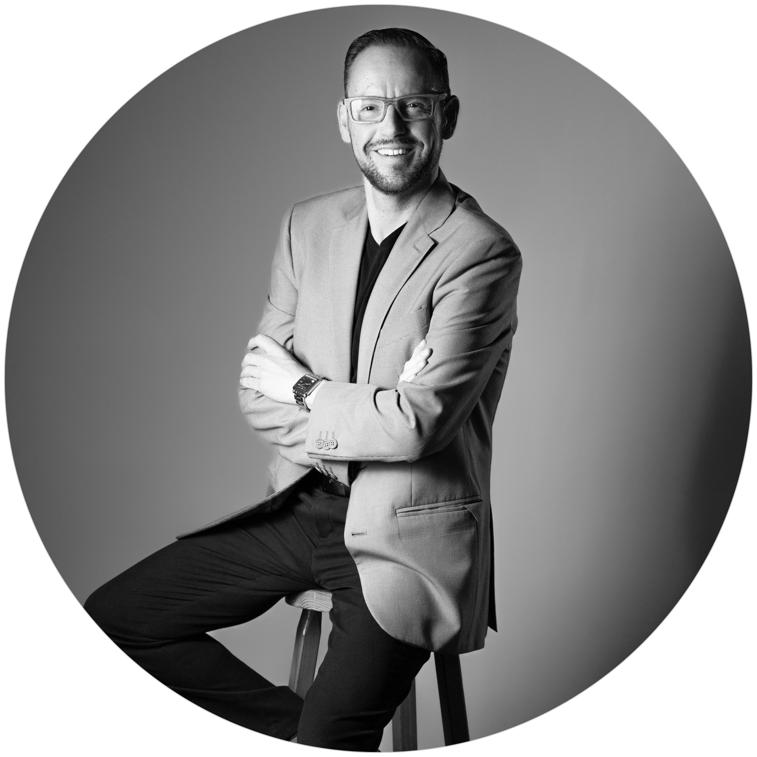 Professional man in blazer smiling with arms crossed, black and white portrait photo.