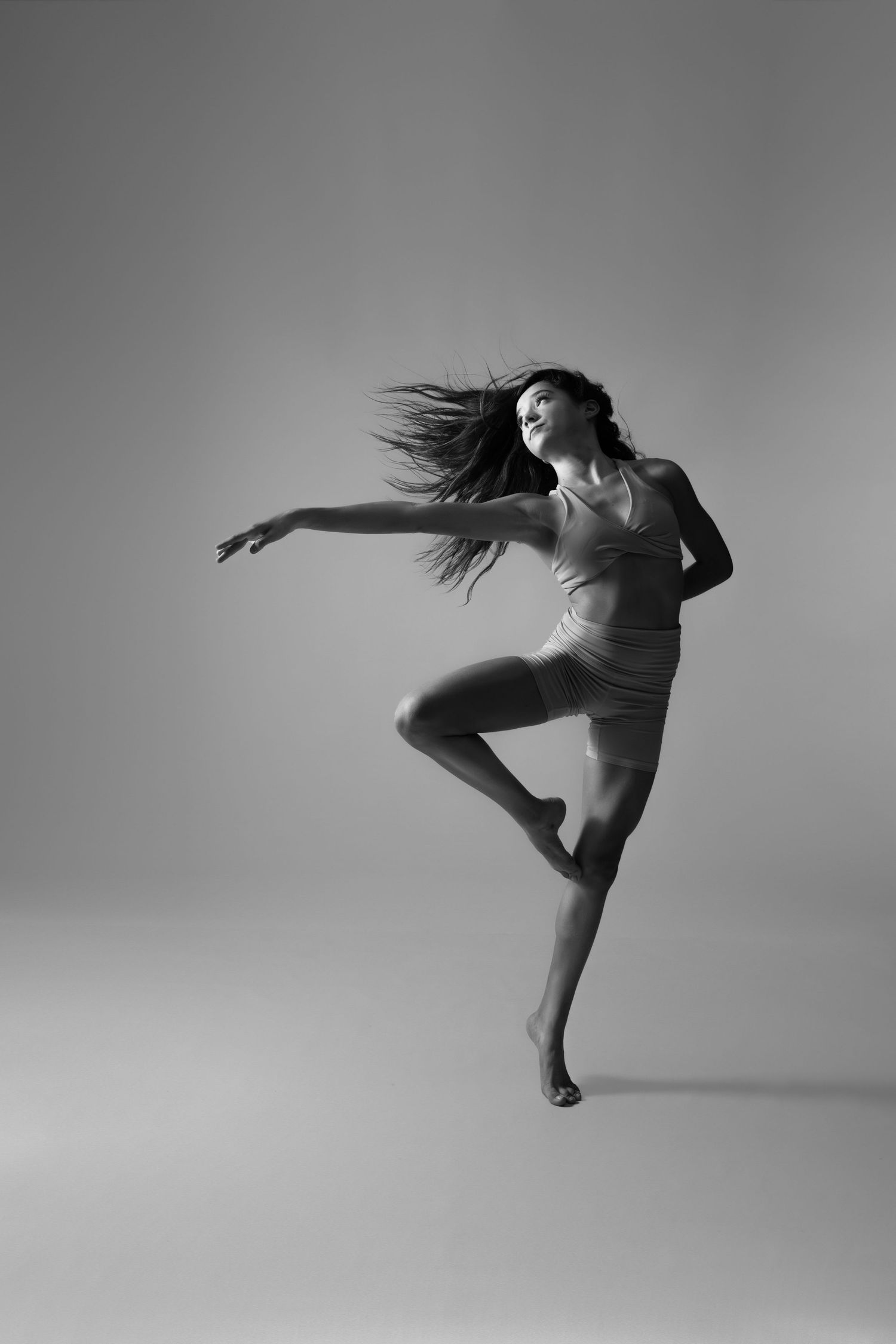 Black and white photo of a graceful female dancer leaping mid-air with flowing hair and extended arms.
