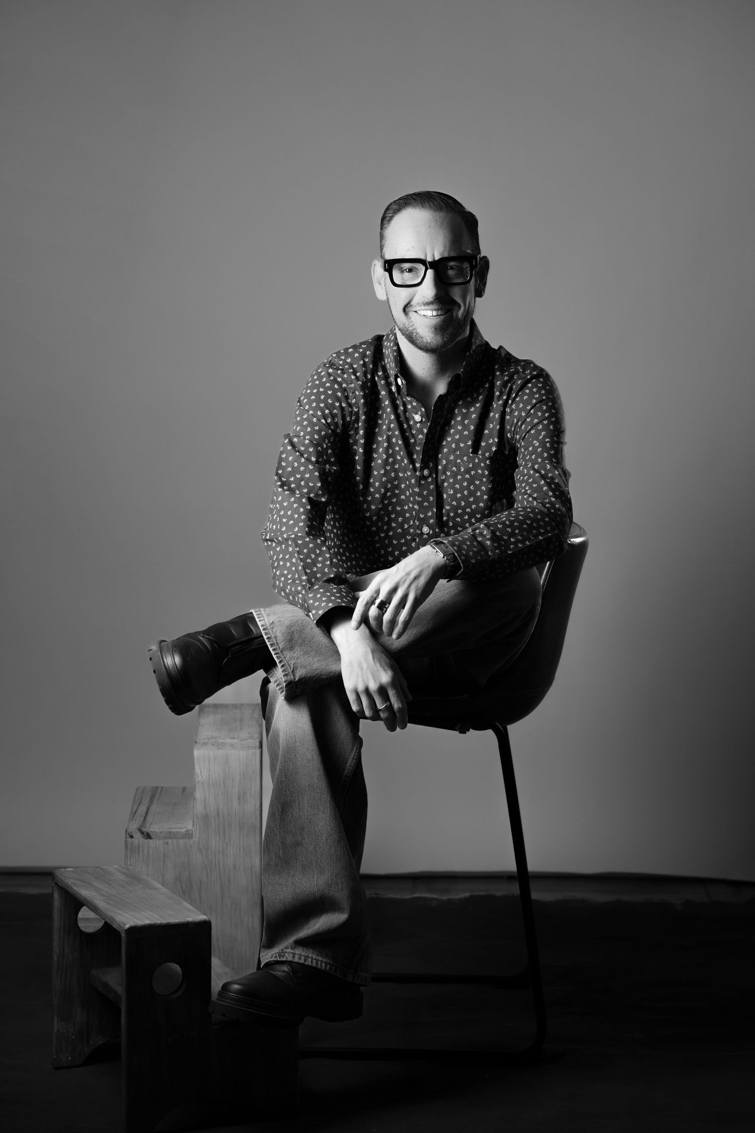 Artistic black and white portraits featuring a person in patterned shirt seated on wooden furniture.