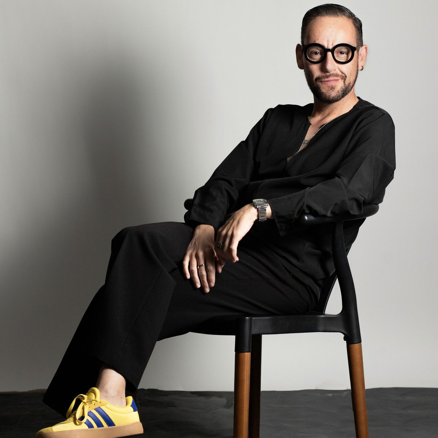 Person in black attire sitting on wooden chair in various poses against white background.