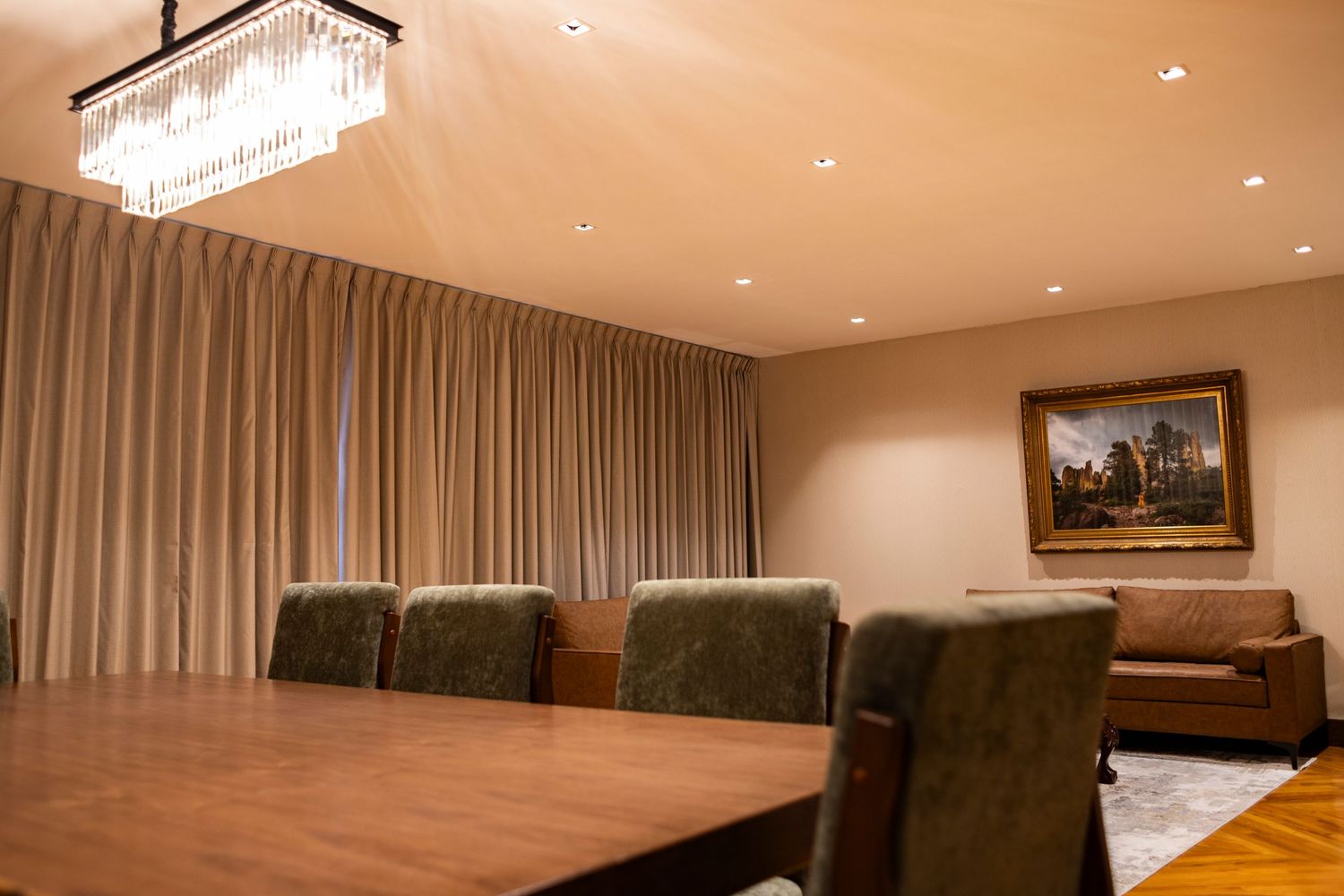 Elegant conference room with wooden table, green velvet chairs, crystal chandelier, beige curtains, and classic landscape painting.