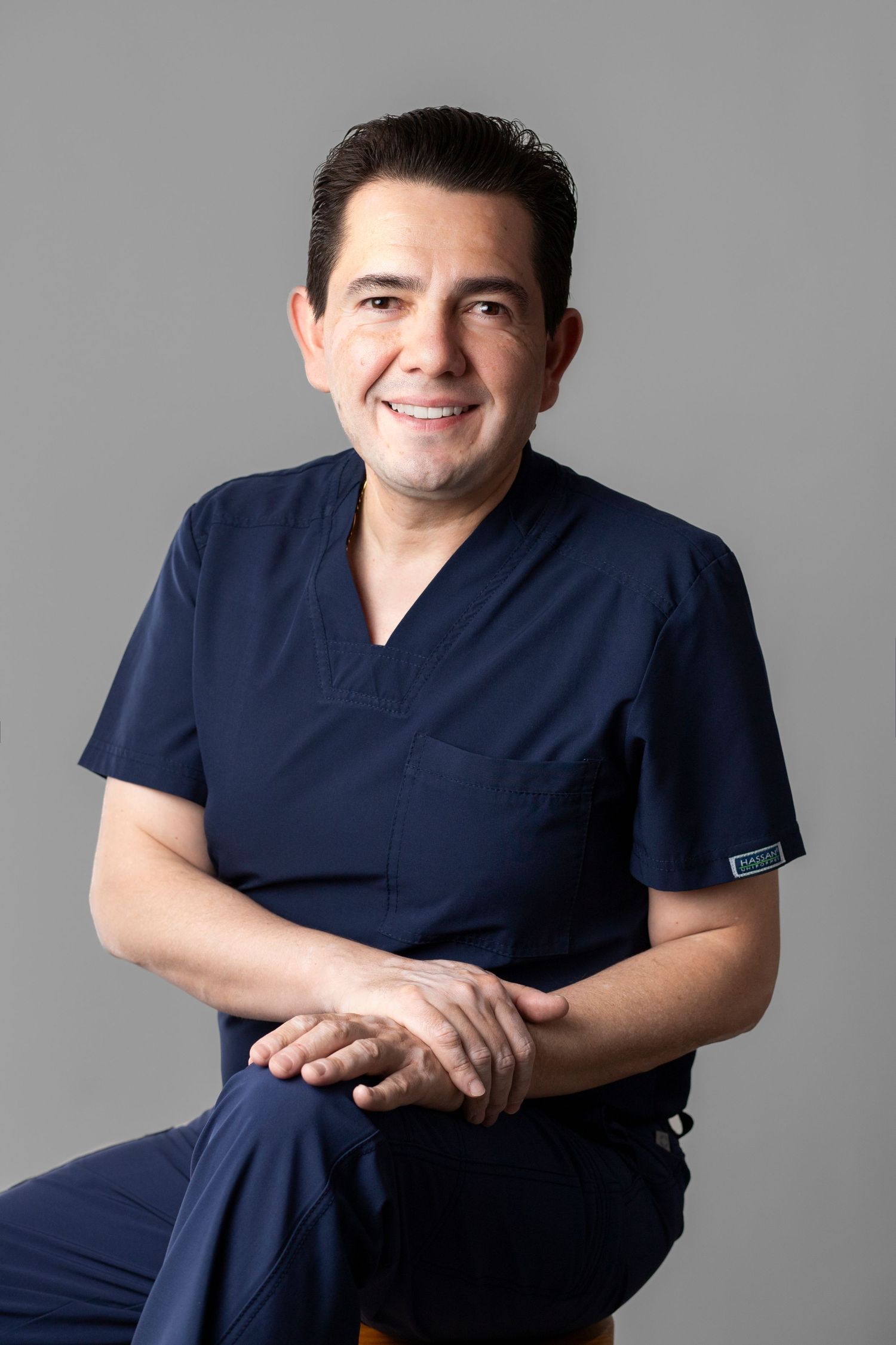 Healthcare professional in navy blue scrubs shown in multiple poses against a gray studio background.
