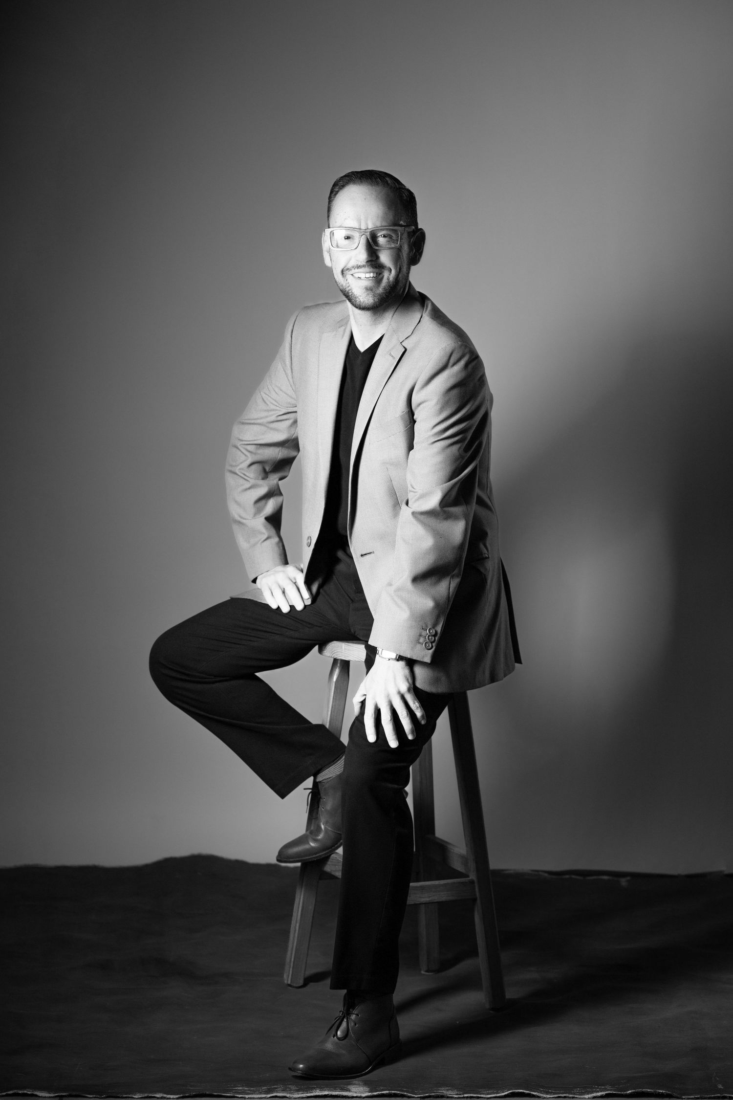 Black and white studio portraits showing a person in a light jacket seated on a chair against dark background.
