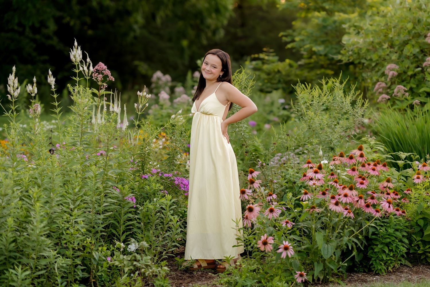 Woman in yellow maxi dress posing among colorful garden flowers including coneflowers and wildflowers.