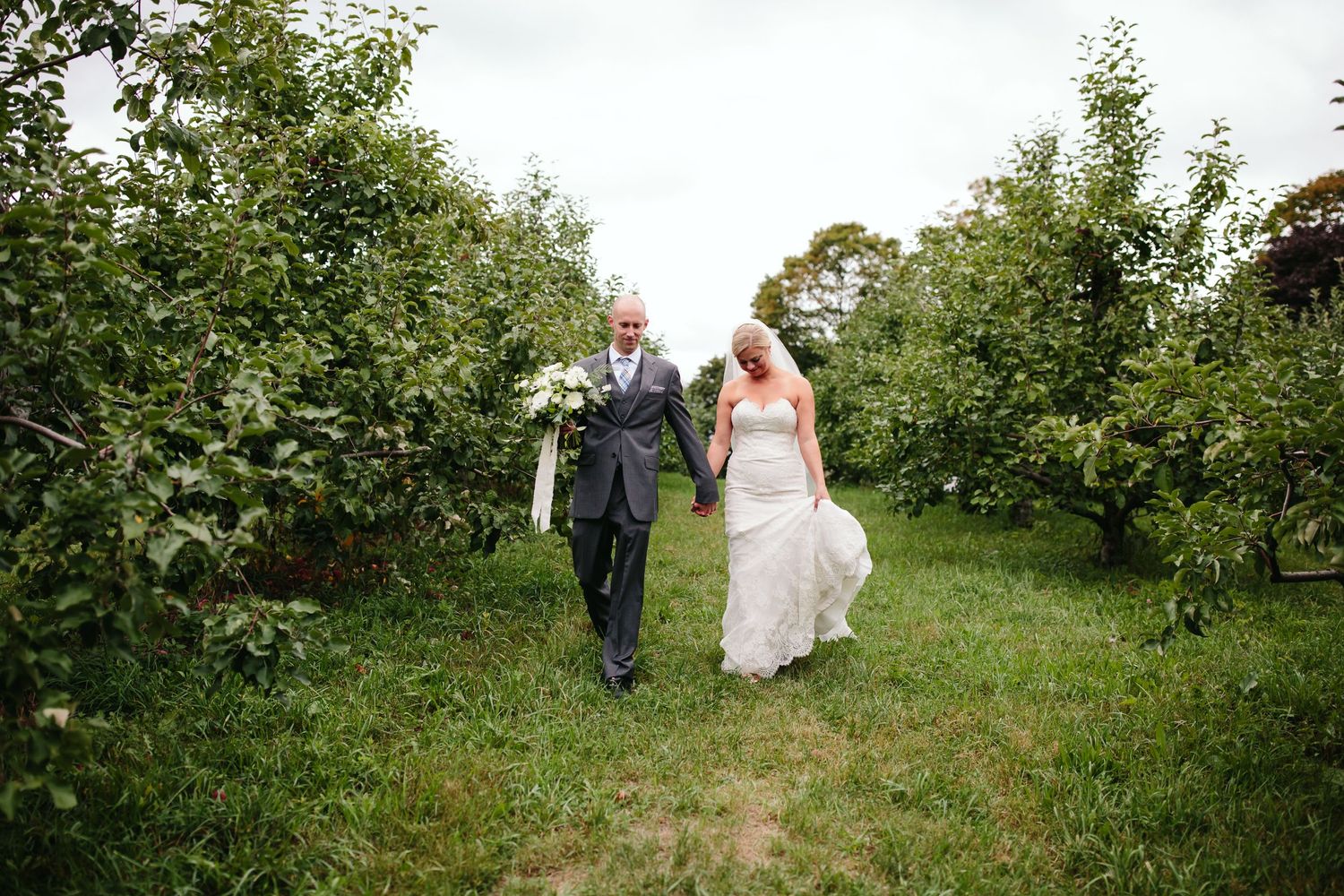 A couple walks together through an orchard path on their wedding day.