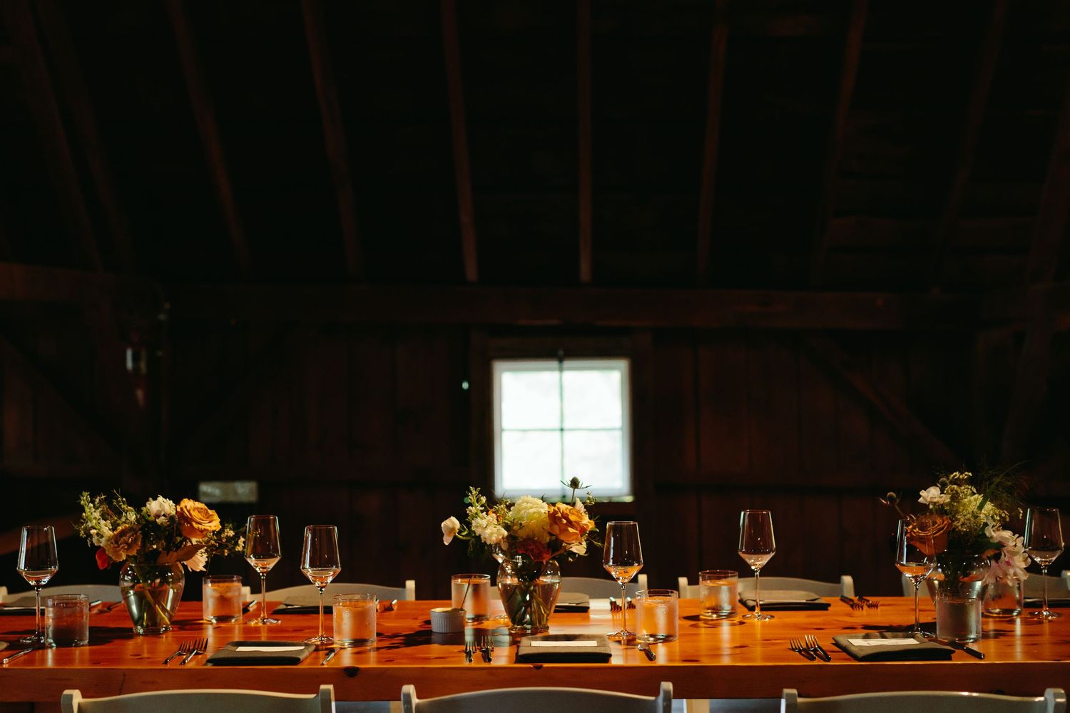 Elegant wedding reception table setting with floral centerpieces and candlelight in a rustic barn venue.