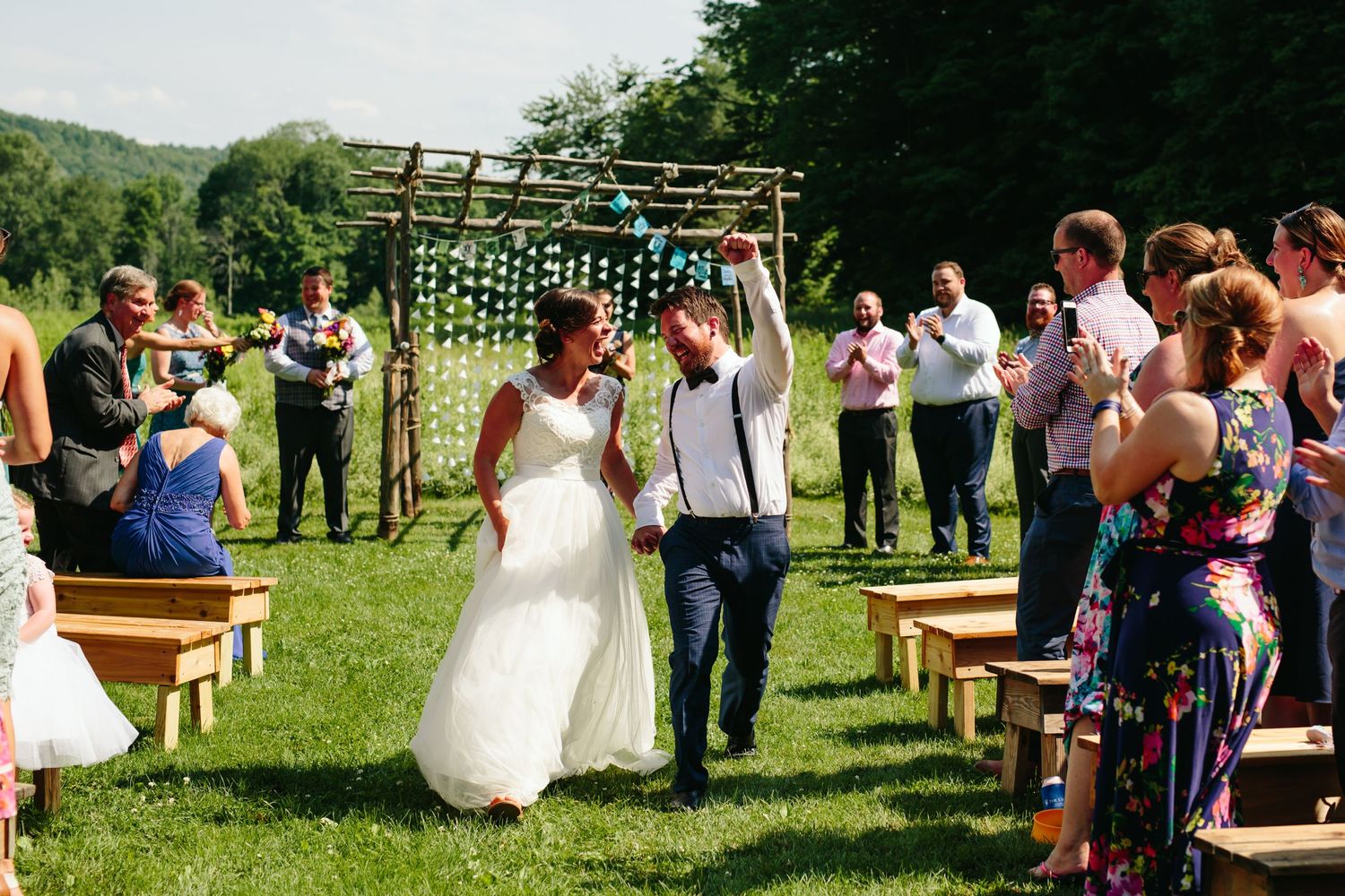 A celebratory recessional down a rustic outdoor aisle with wooden arch and cheering guests at Lareau Farm Inn - Waitsfield, VT