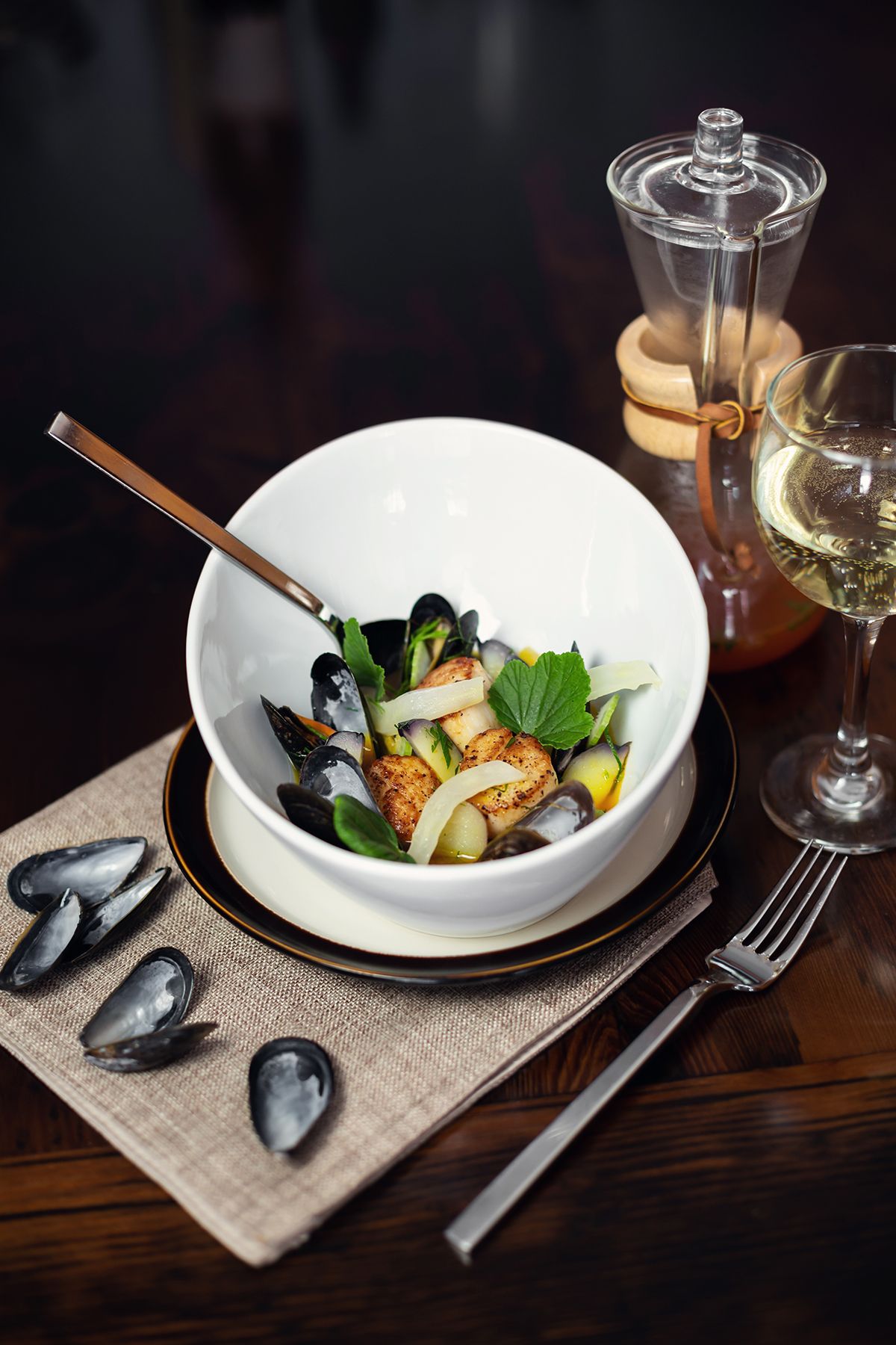 Fresh mussels and seafood dish plated elegantly on white ceramic plates with garnish and wine glass on rustic table setting.