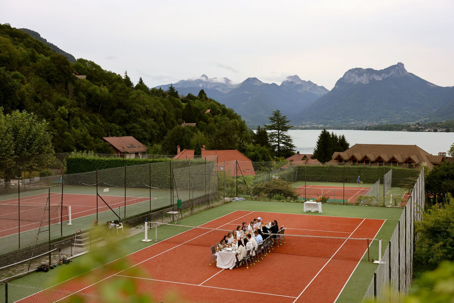 Wedding party dining on a tennis court with stunning Alpine lake and mountain views in the background.