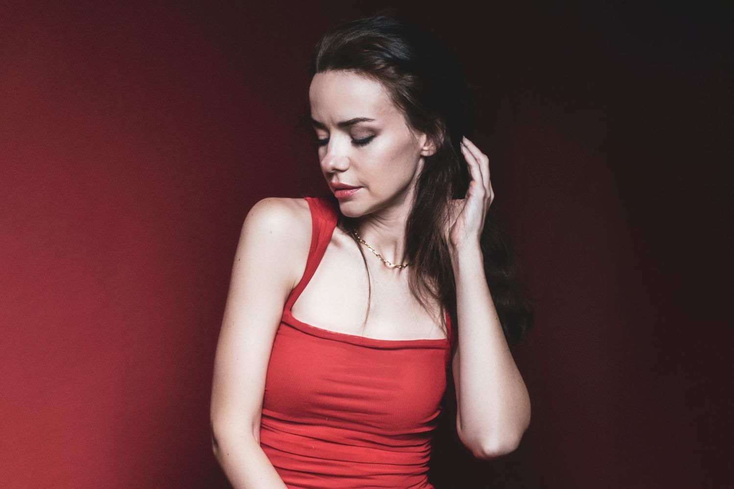Woman in red dress poses dramatically against dark background in artistic portrait series.