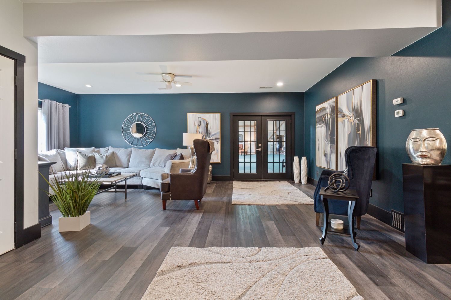 Modern living room with teal blue walls, hardwood floors, French doors, and contemporary furnishings in an open layout space.