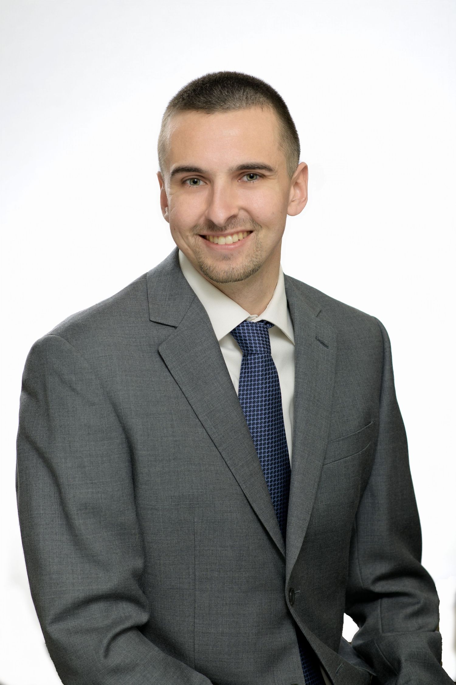 Professional headshot of someone in a grey suit and blue tie against a white background.