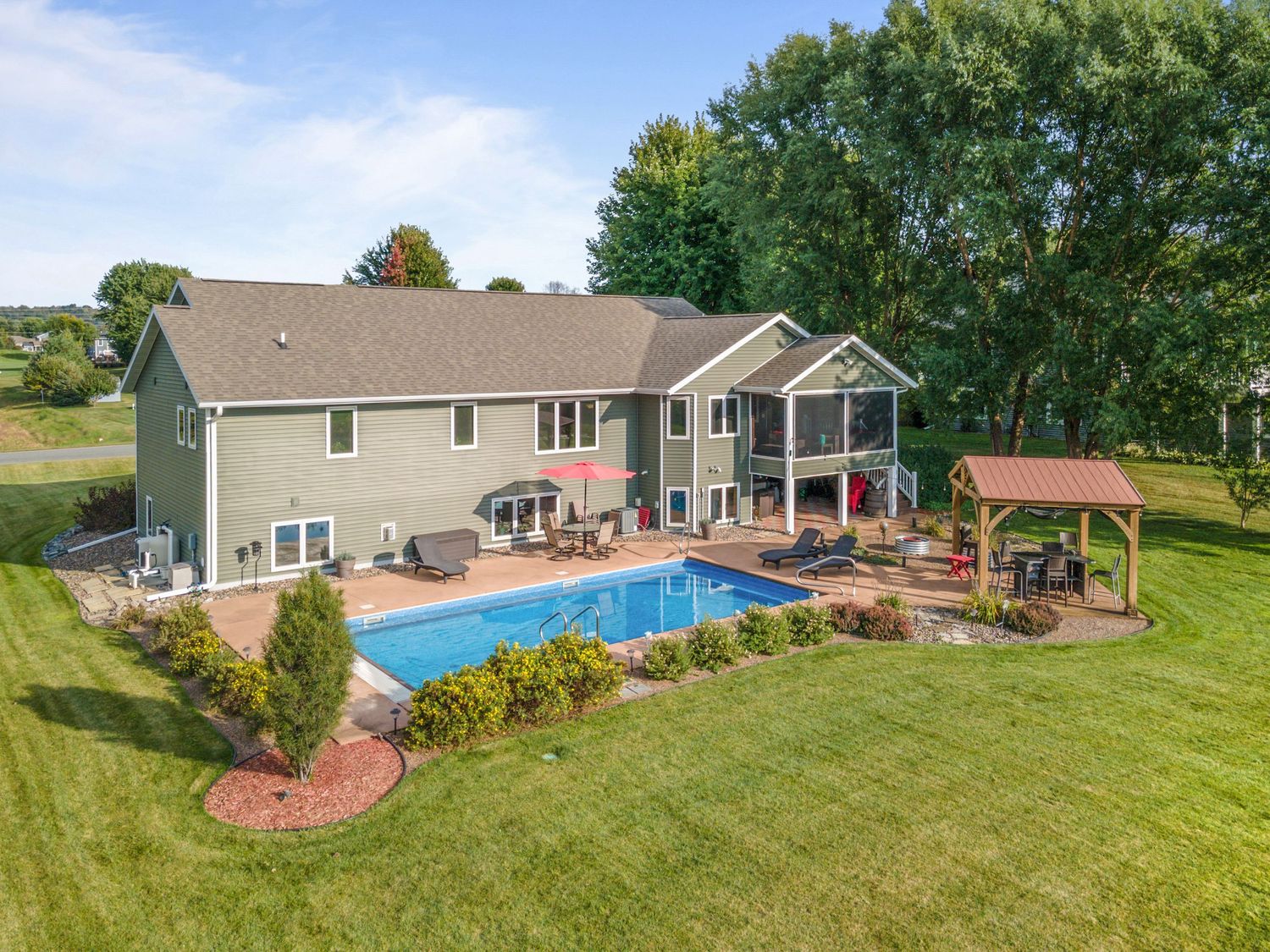 Aerial view of modern suburban house with inground swimming pool, landscaped yard and covered patio gazebo in backyard.