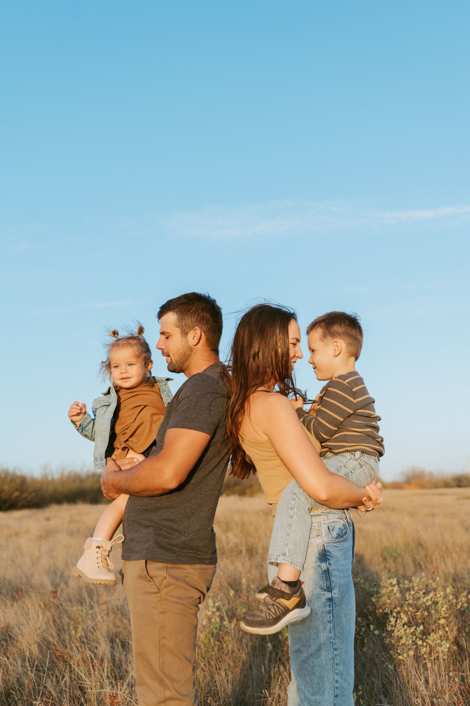 Family portrait with young children standing in a golden field at sunset.