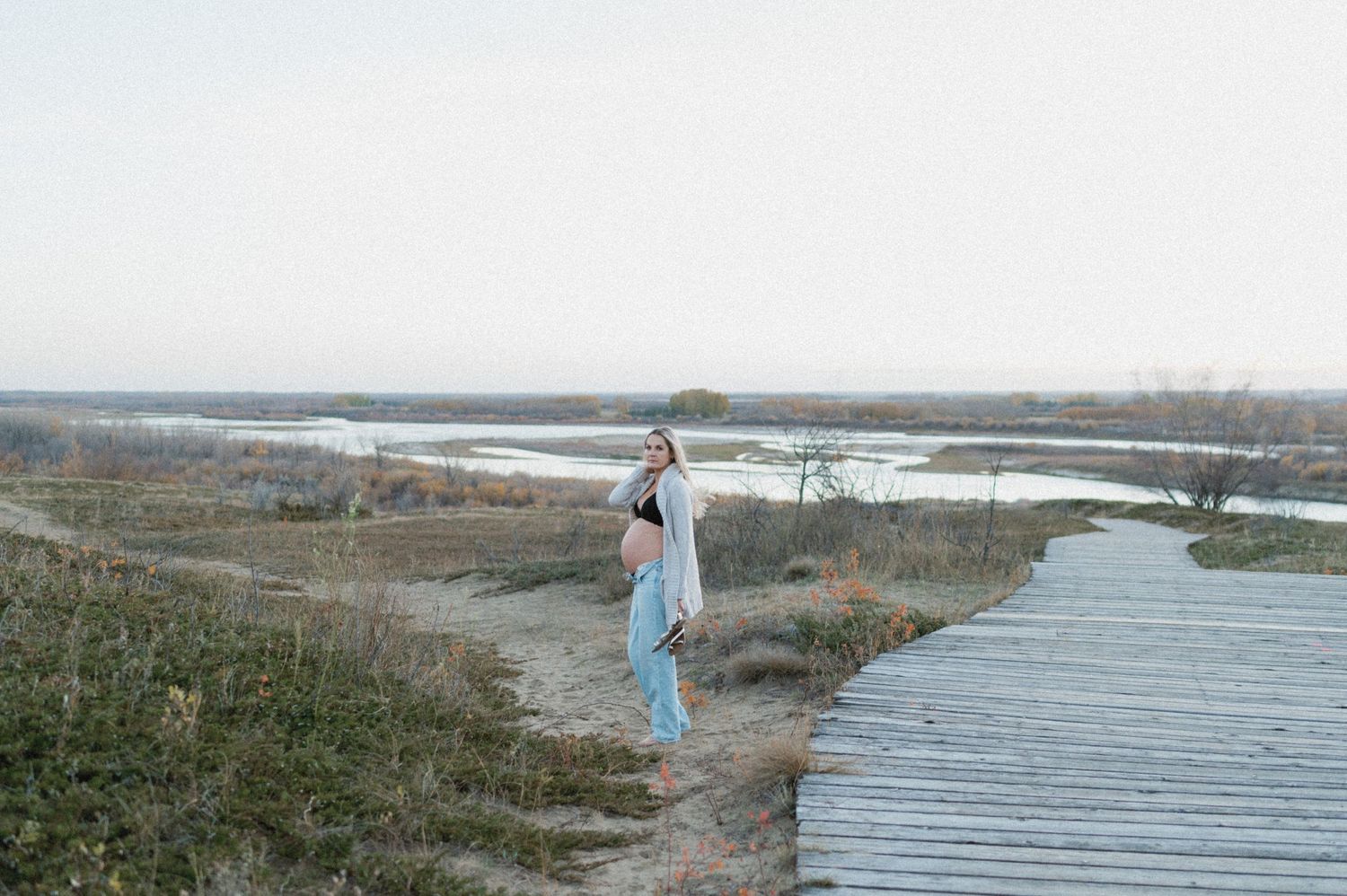 Person standing on wooden boardwalk overlooking scenic marsh landscape.