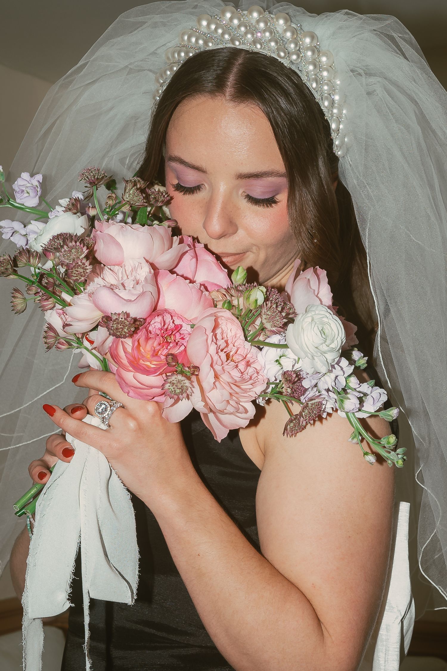A bride in white veil and pearls smells a lush pink and white bouquet of roses and flowers.