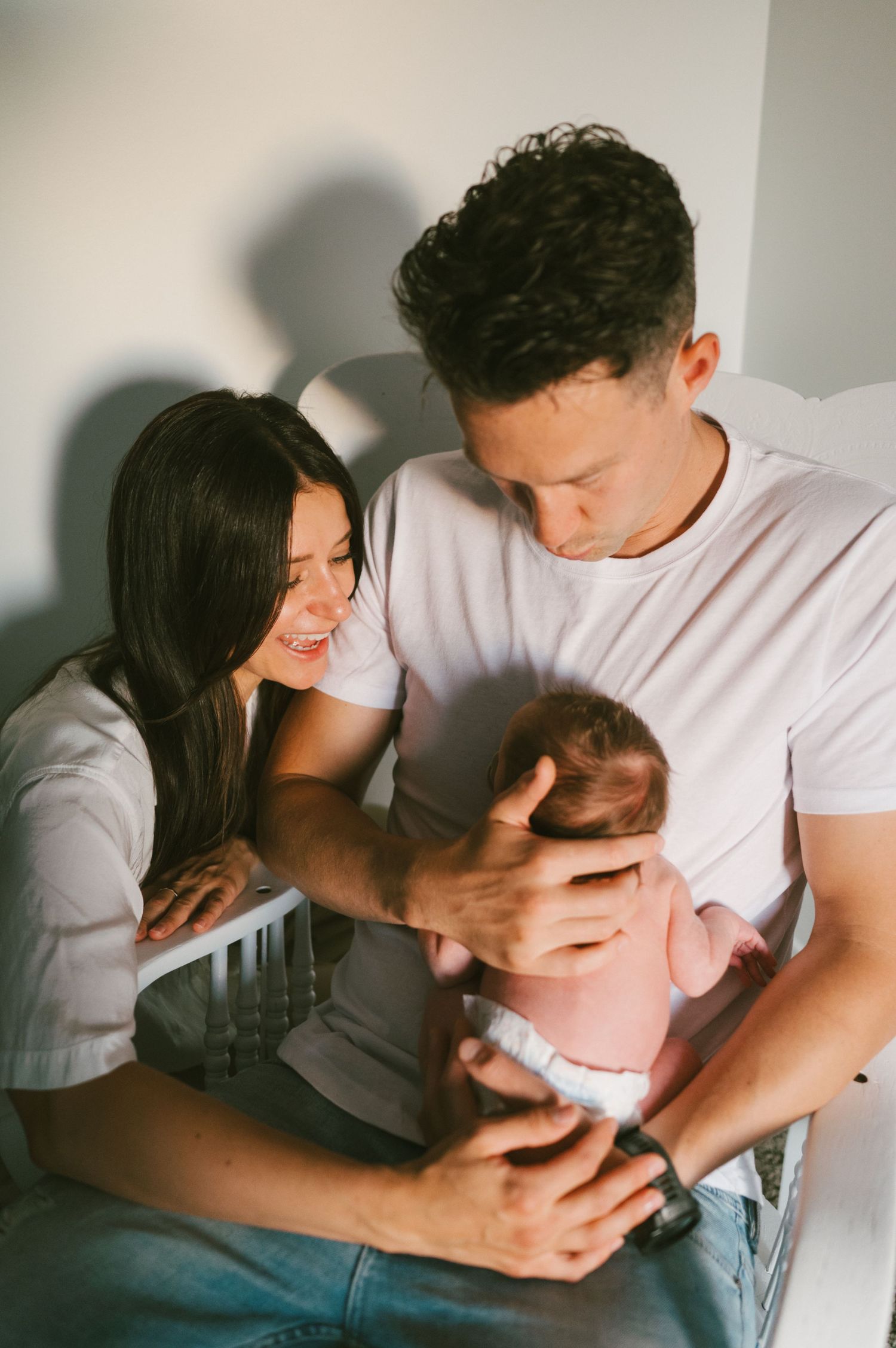 Parents sharing tender moment while holding newborn baby in nursery chair.