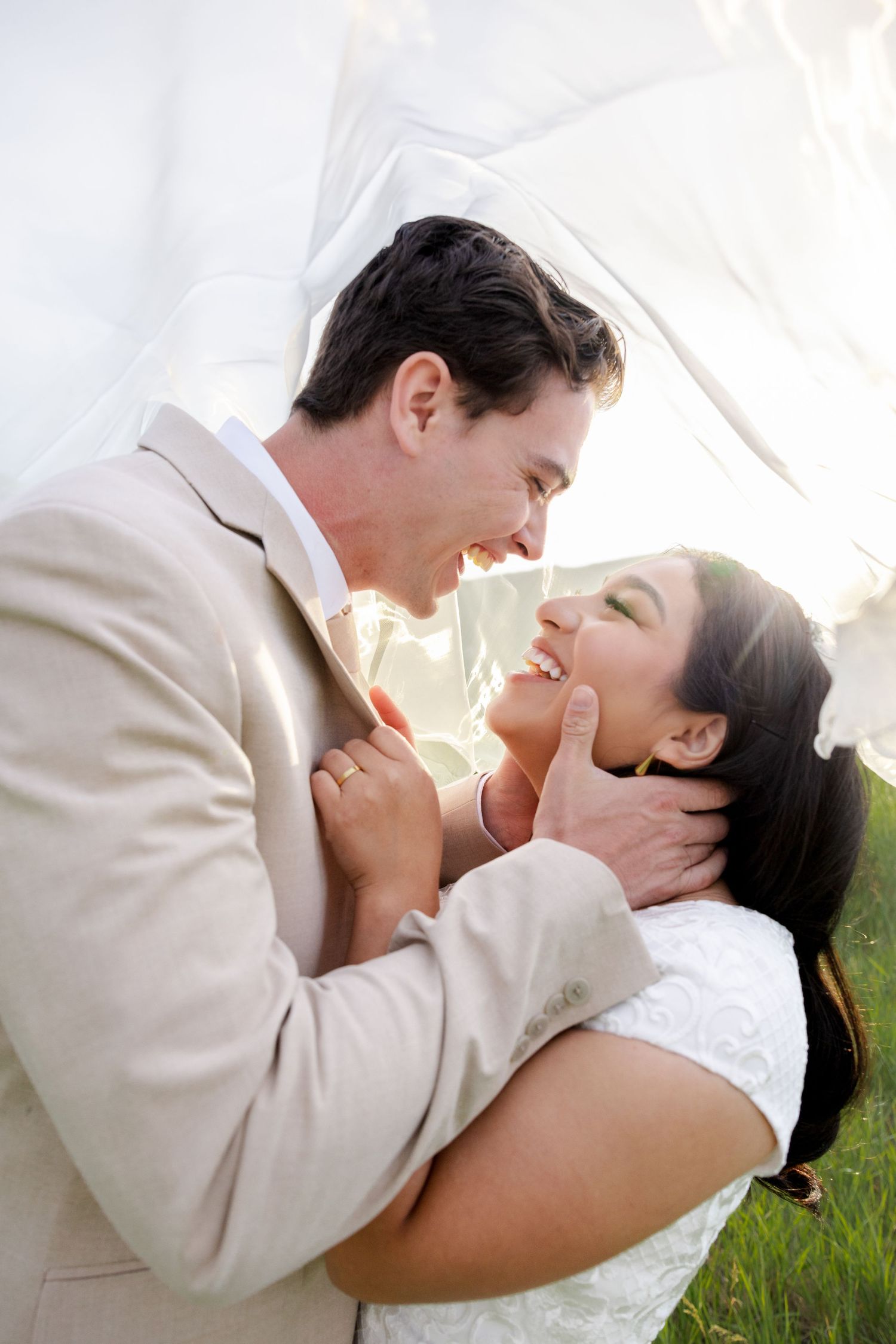 Close-up of bride and groom smiling at each other while posing under a veil during their bridal session in Salt Lake City, Utah.