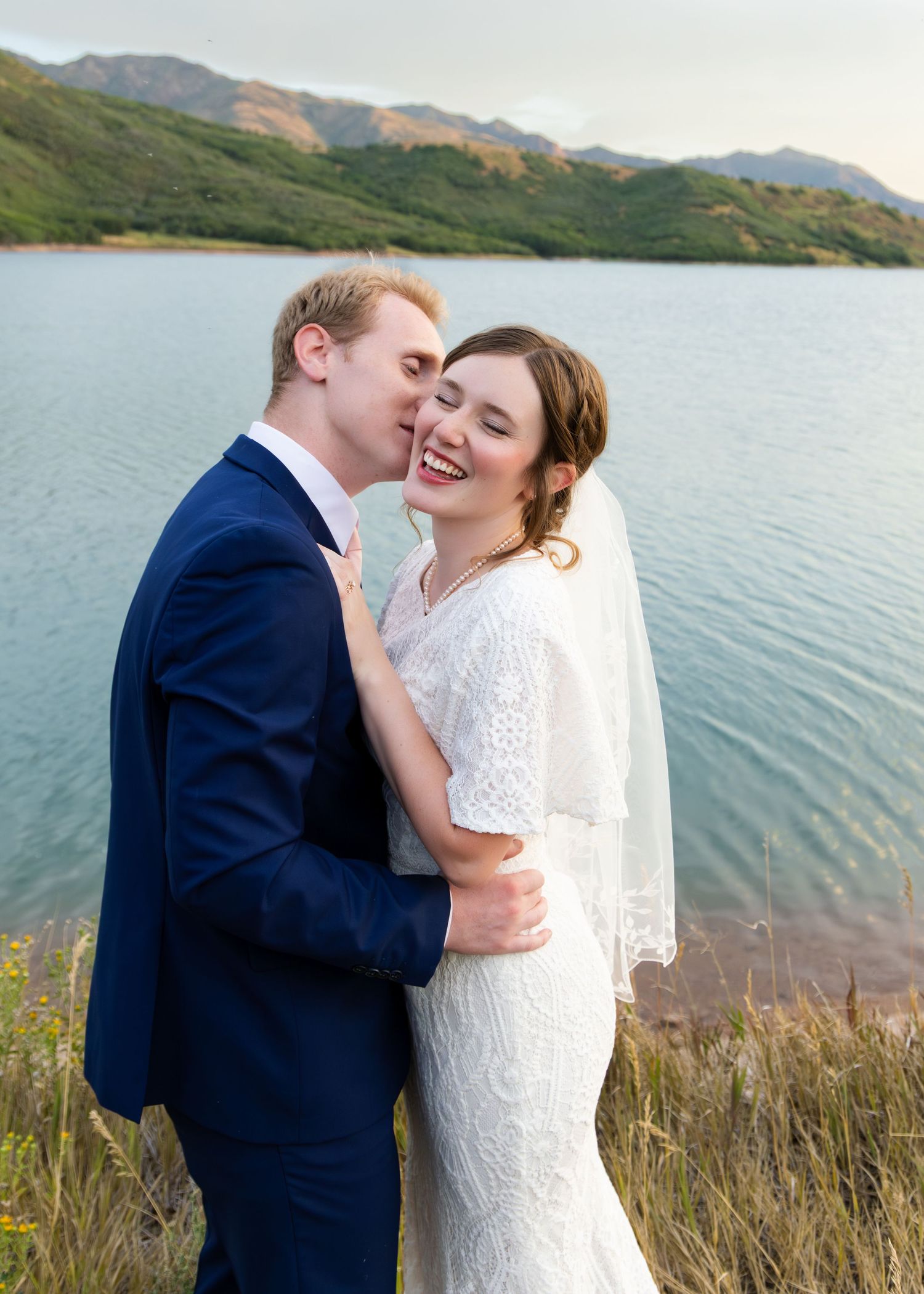 Groom kissing the bride on her cheek while she laughs during their first look in Park City Canyon, Utah