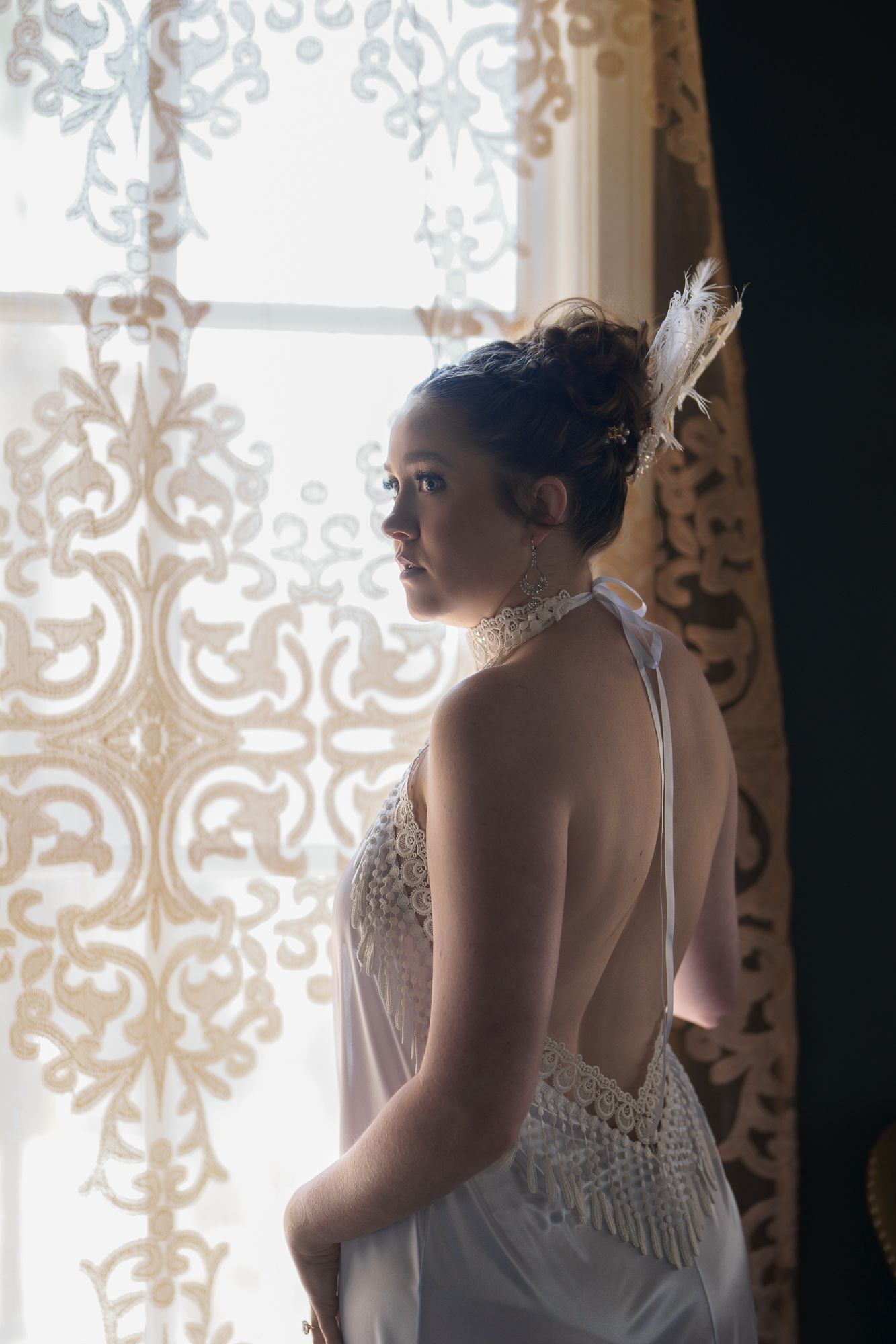 Ethereal silhouette against ornate lace curtains in vintage-inspired bridal shoot.