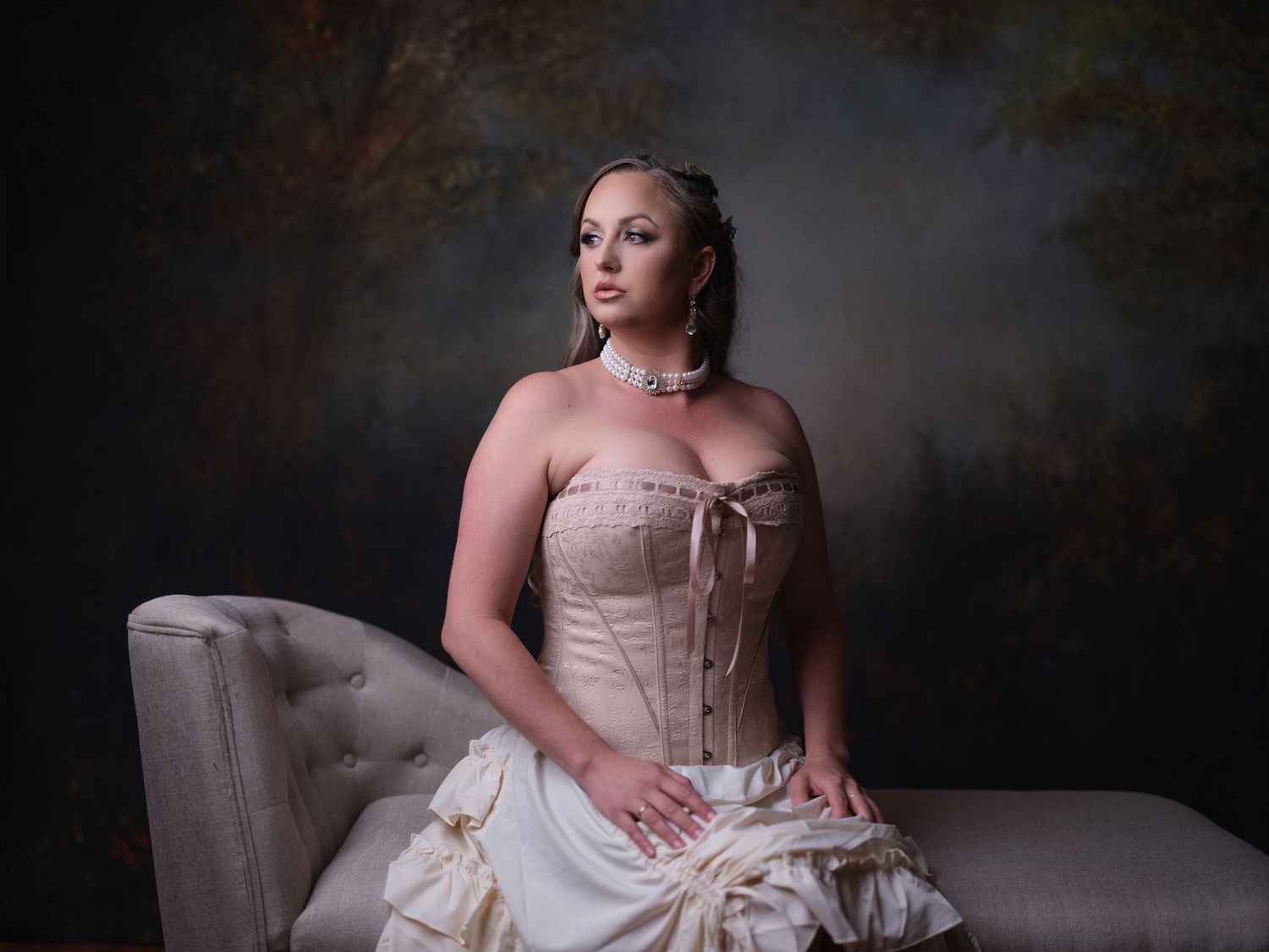 Elegant boudoir session featuring corset dress and vintage furniture against dark backdrop.