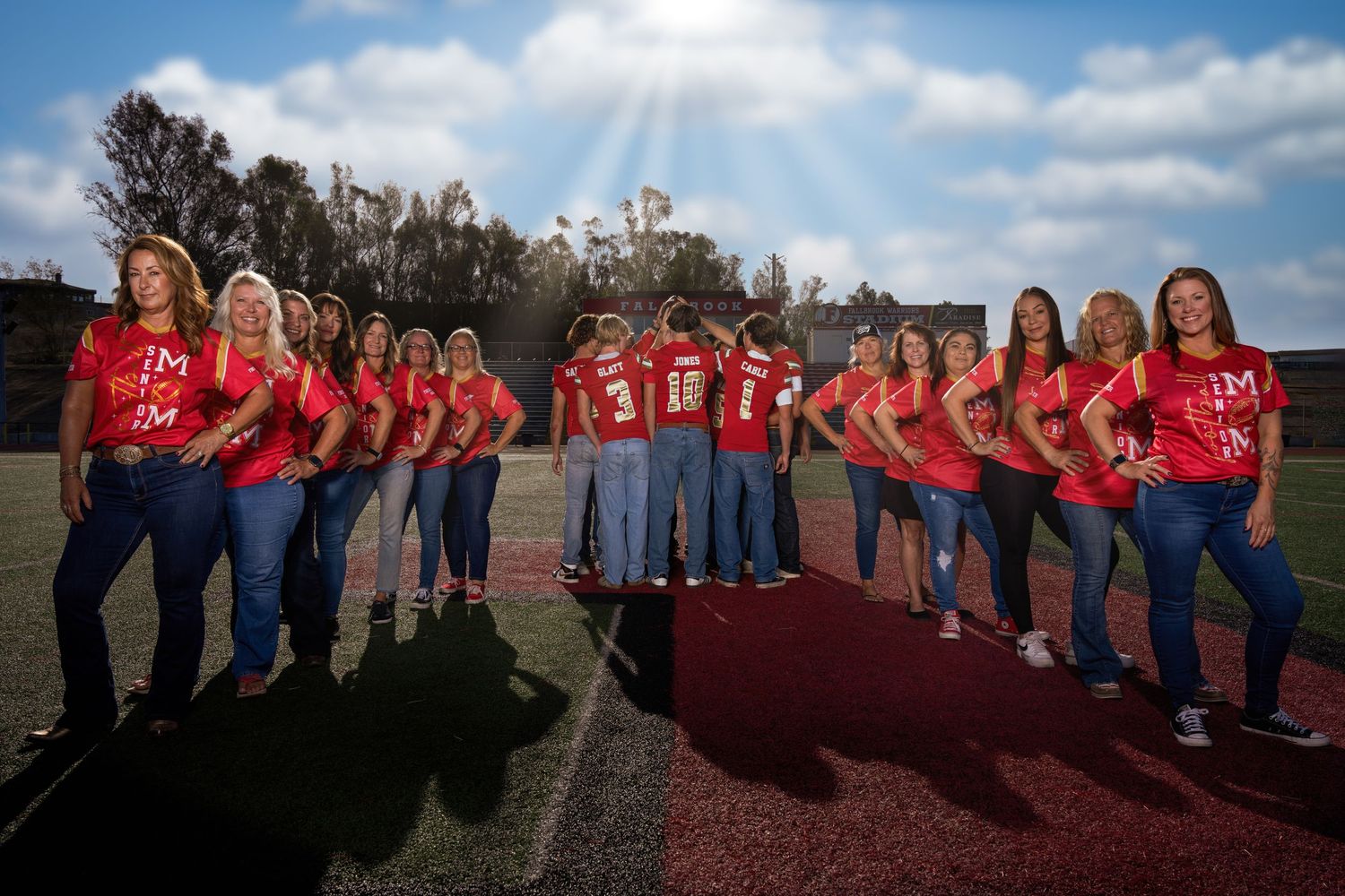 Group of people in matching red shirts and jeans stand together for a casual outdoor photo shoot.