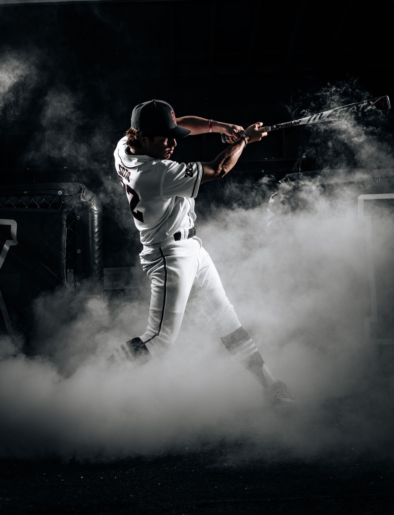 Baseball player emerges dramatically through white smoke during game entrance in dramatic black and white composition.