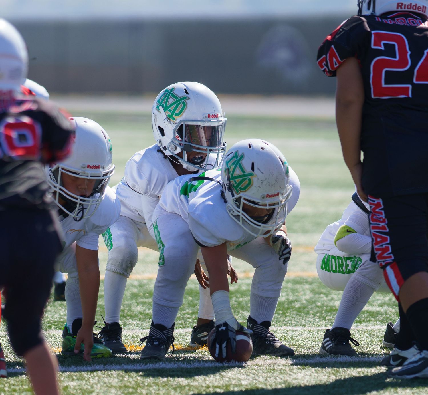 Football players line up at scrimmage during a game on a grass field with white and black uniforms.