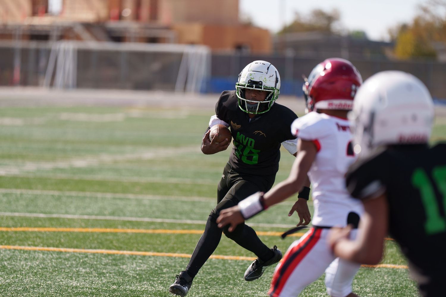 Football player in dark uniform runs with ball while opponent in white and red uniform attempts defensive play.