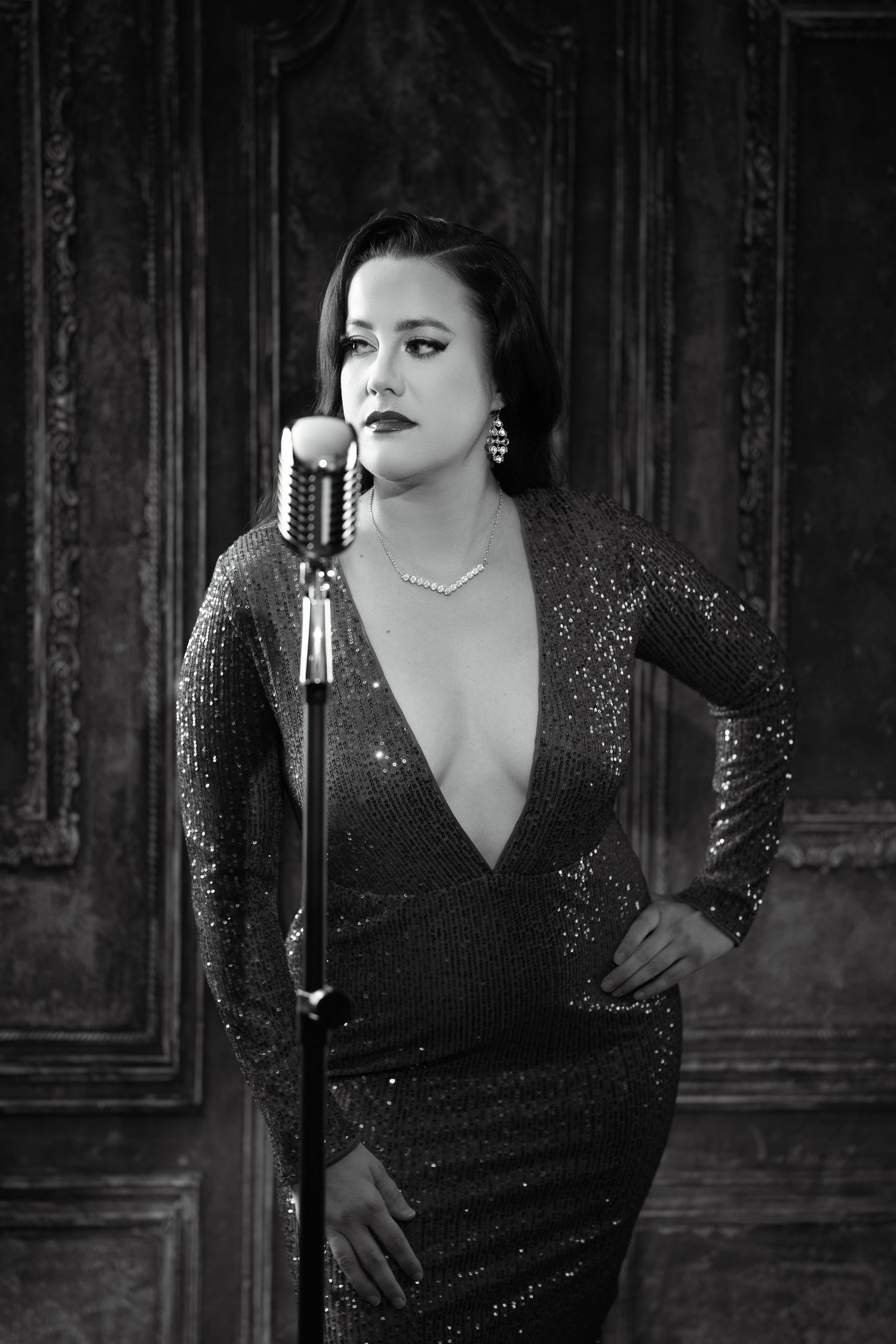 Black and white photo of a glamorous woman in sequin dress at vintage microphone stand.