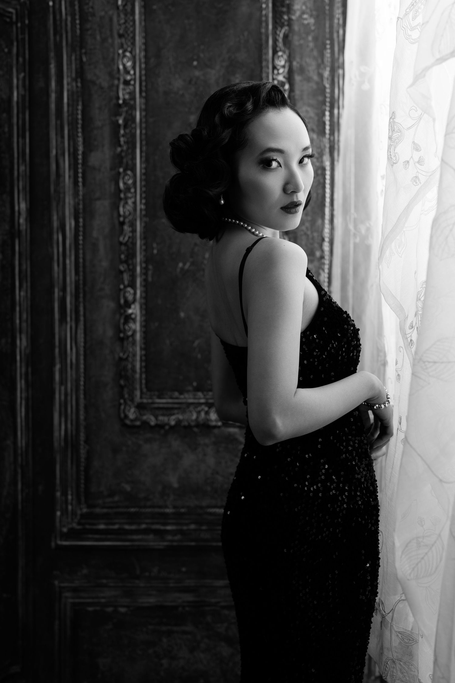 Dramatic black and white boudoir photo series featuring sparkly black dress and sheer curtains.