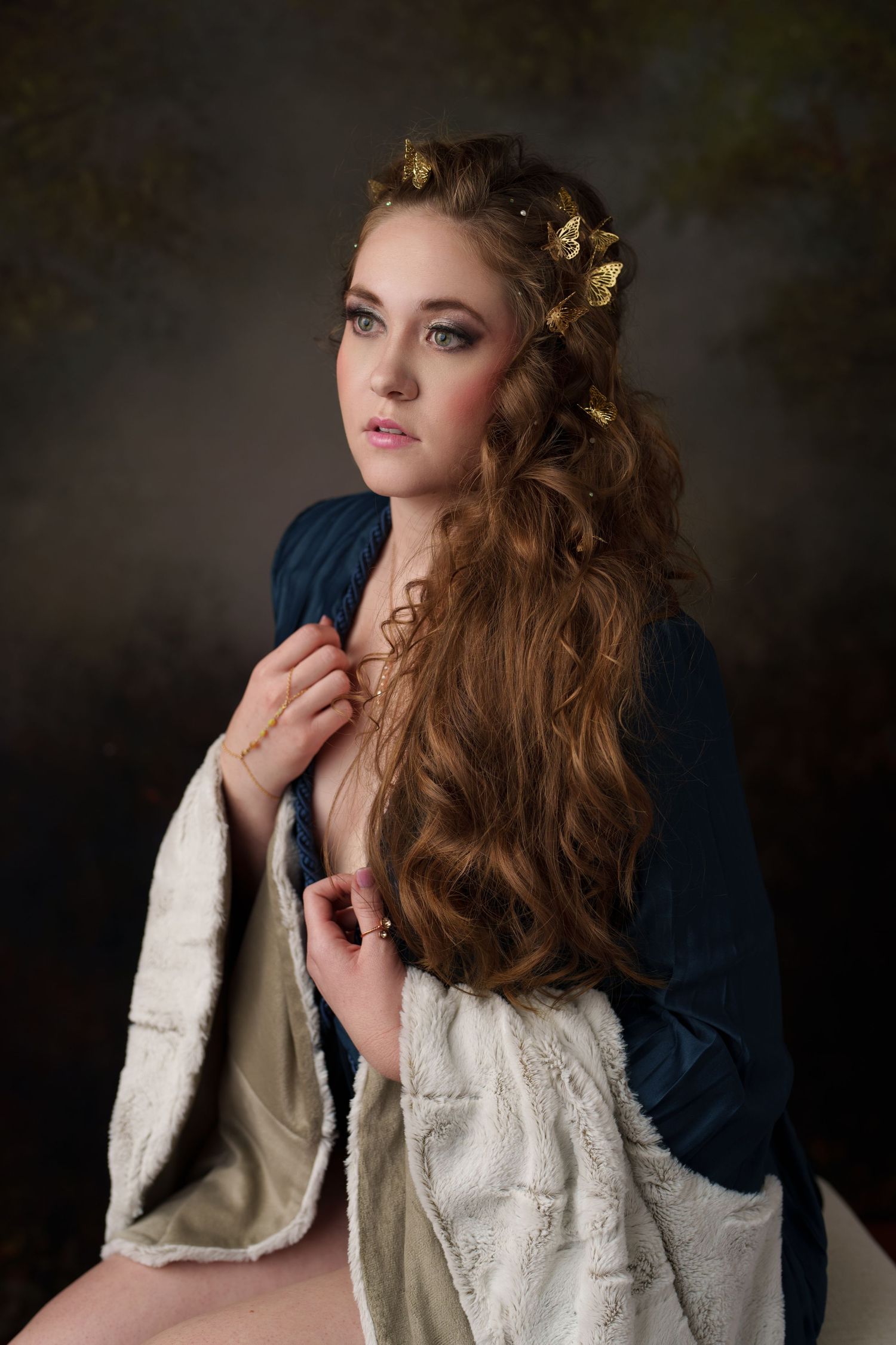 Young woman with long curly hair adorned with gold butterfly clips, wearing a blue velvet and fur wrap.