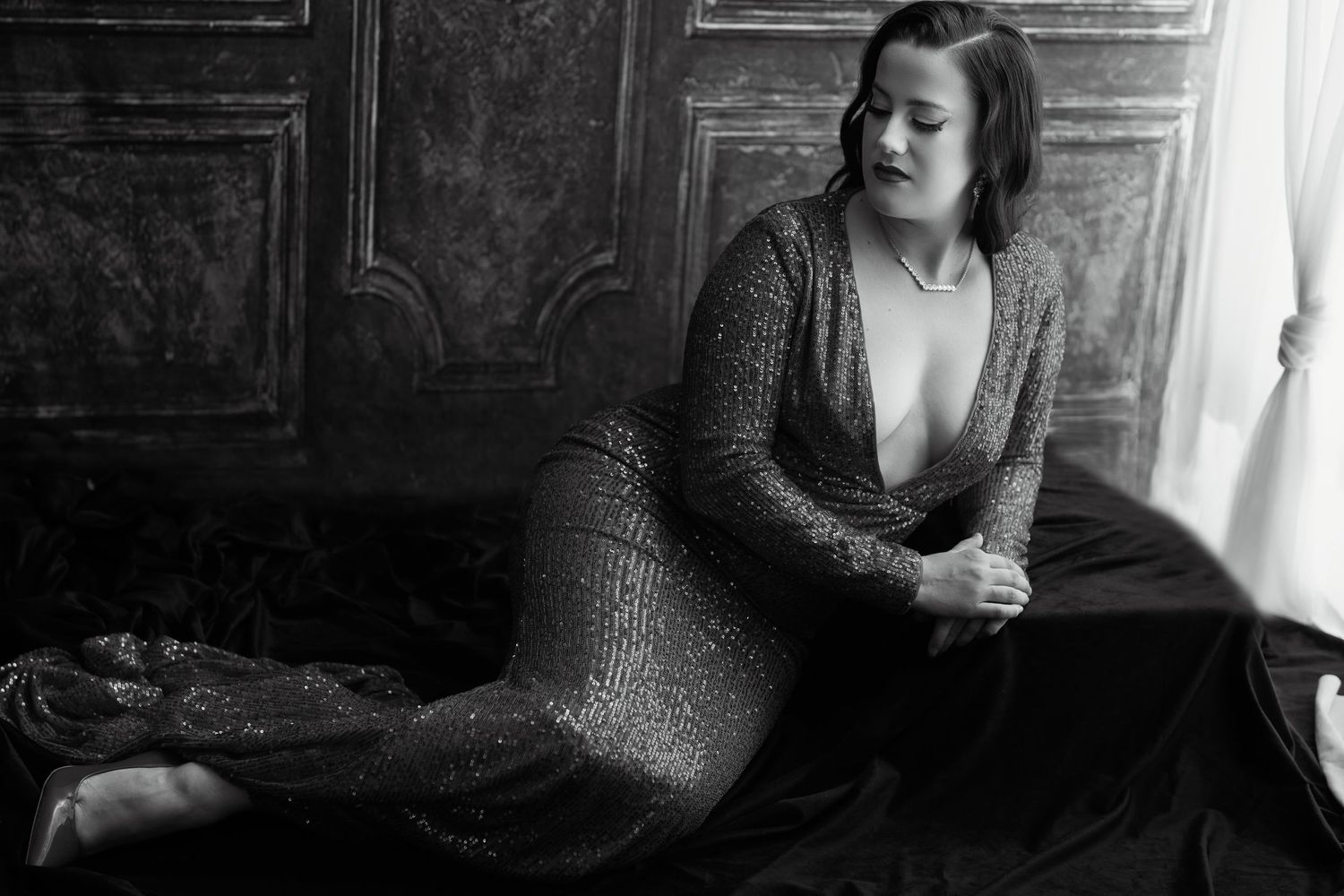 Black and white photo of a woman in a sequined gown posing elegantly on the floor near ornate wooden doors.